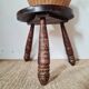 Small brutalist tripod stool made of turned wood.