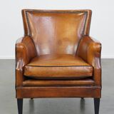 Cognac-colored sheepskin armchair with black piping and decorative nails