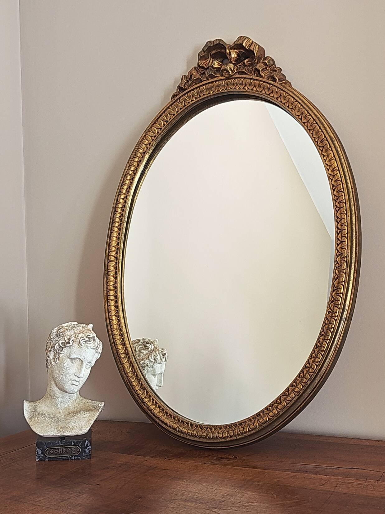 Vintage oval mirror with a carved wooden frame in gold, decorated with a bow.