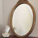 Vintage oval mirror with a carved wooden frame in gold, decorated with a bow.