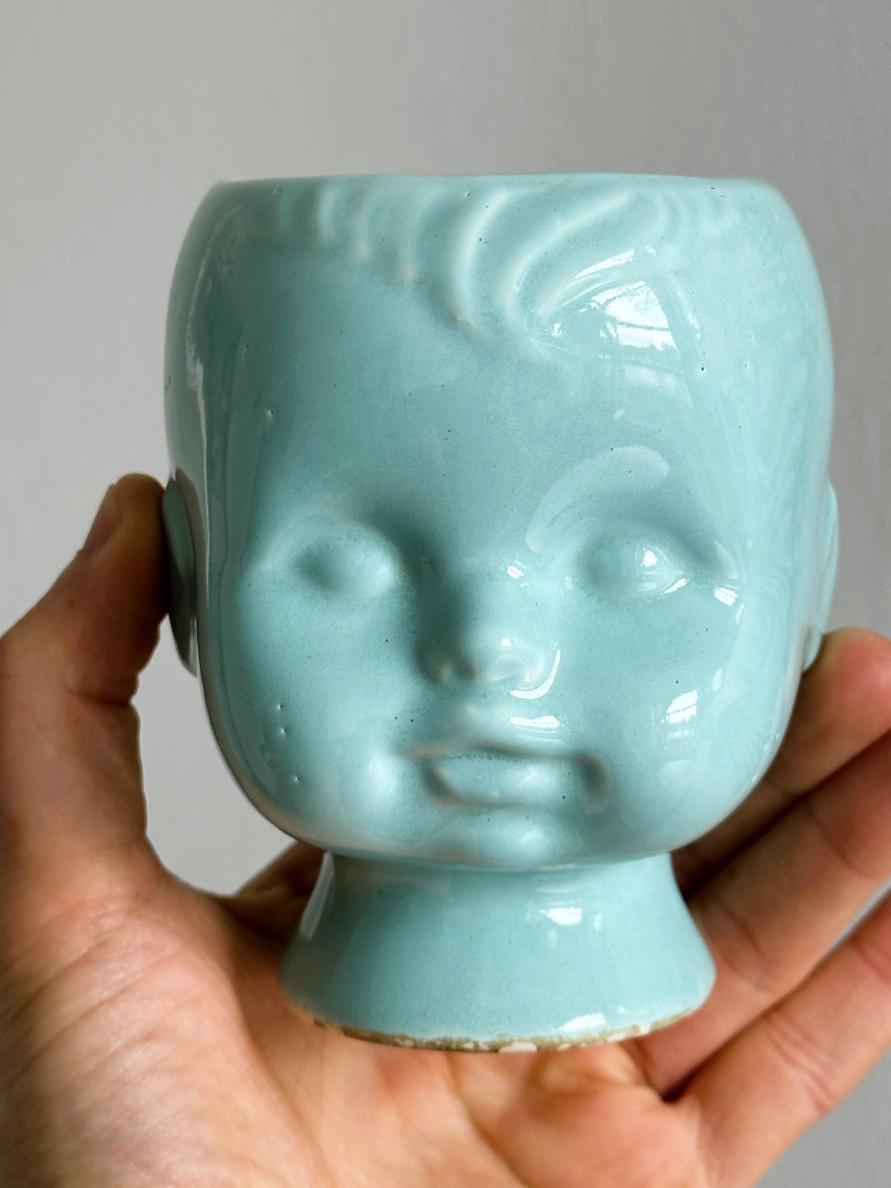 Turquoise plant pot in the shape of a vintage doll's head.