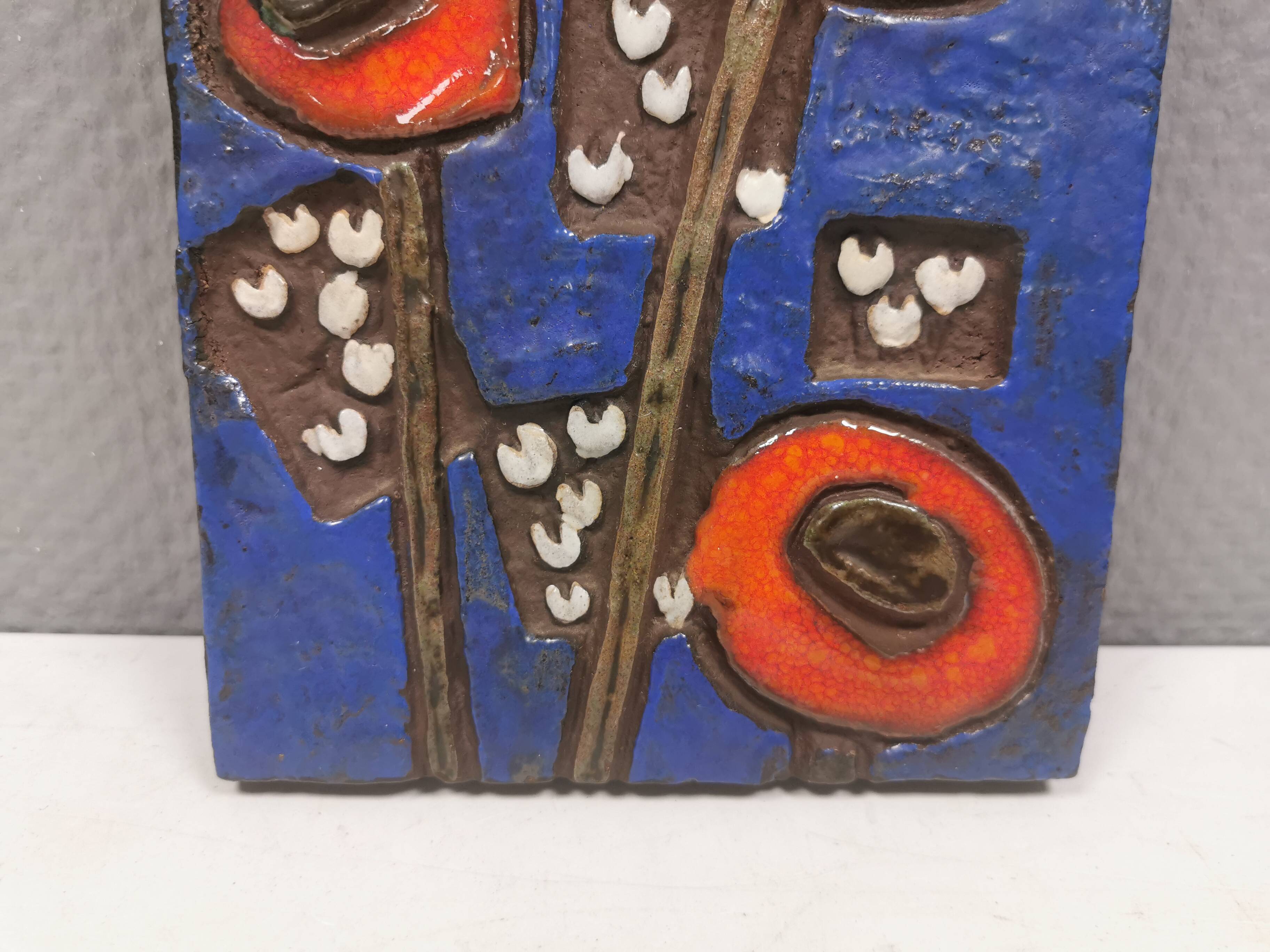 Ceramic relief in attractive blue with a motif of white/red flowers.