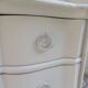 A beautifully crafted crossbow-shaped chest of drawers, finished in pearl grey with a whitewashed top.