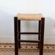 Vintage rustic stool in wood with a straw seat.