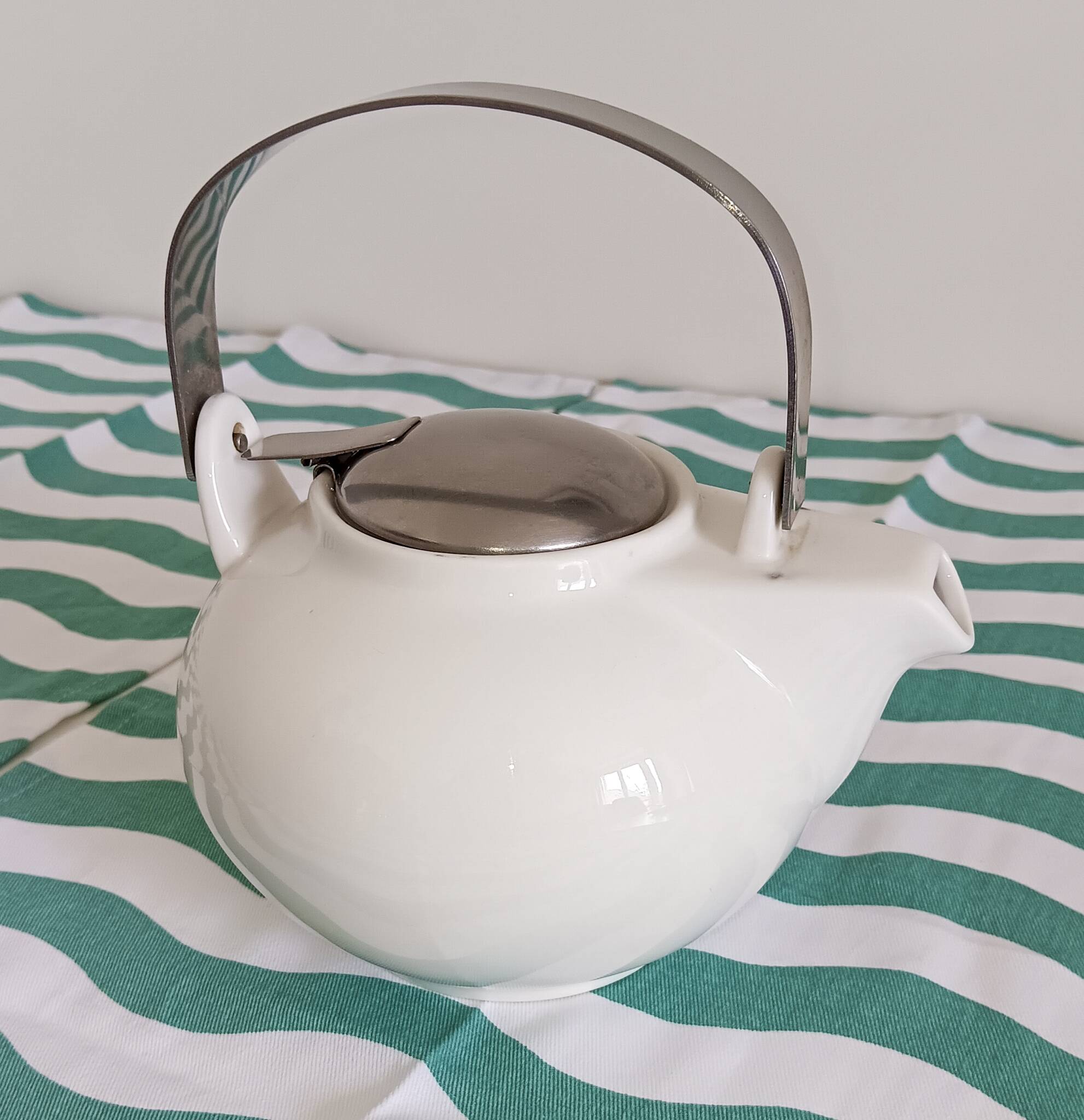 White porcelain teapot. Shiny stainless steel handle and lid