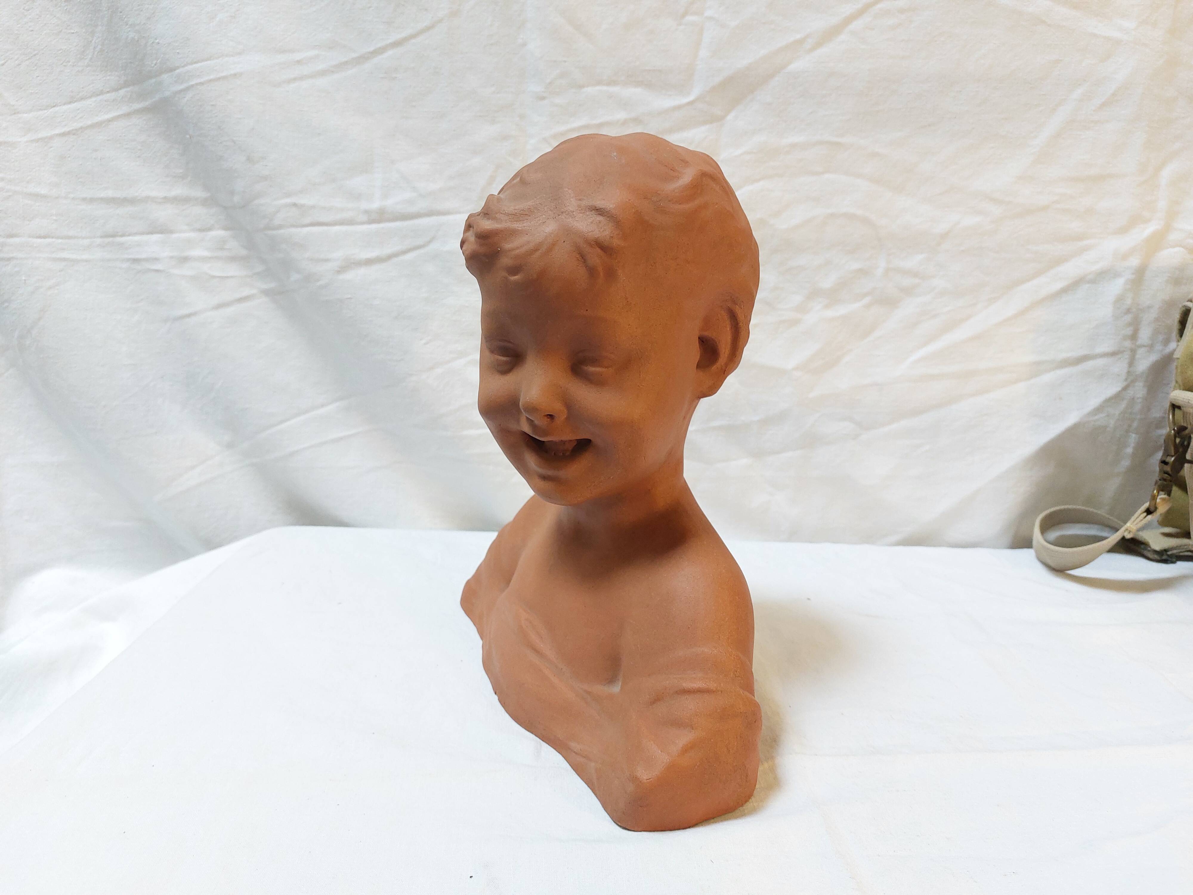 Terracotta bust of a smiling little boy.