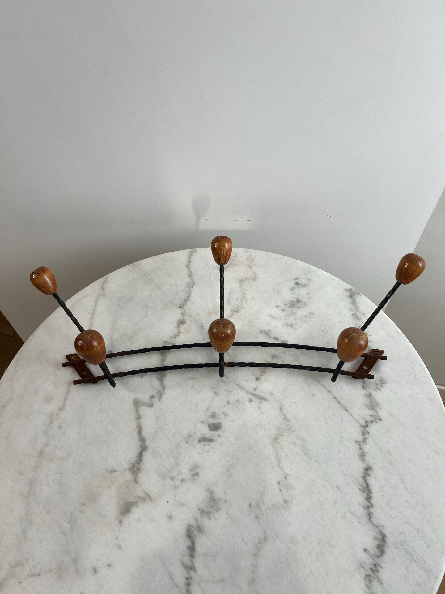 Wall-mounted coat rack in wrought iron with turned wooden knobs.