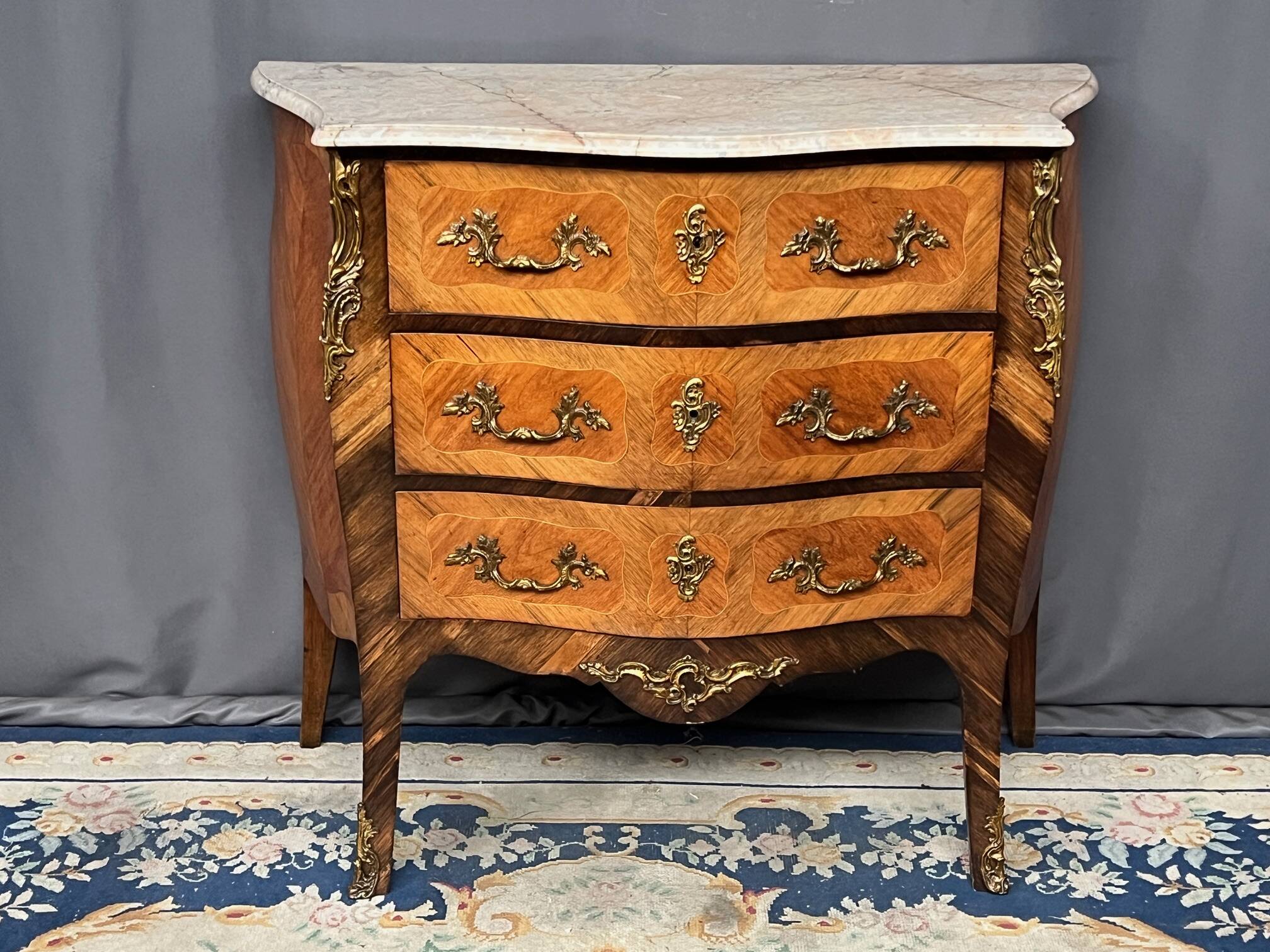 Louis XV style commode with rosewood veneer, gilded bronze mounts, and marble top.