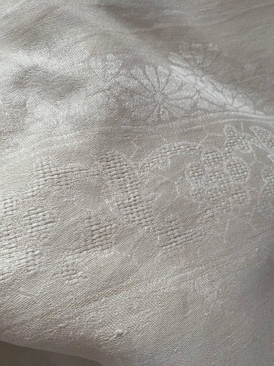 Damask tablecloth with a floral pattern and a central embroidered monogram.