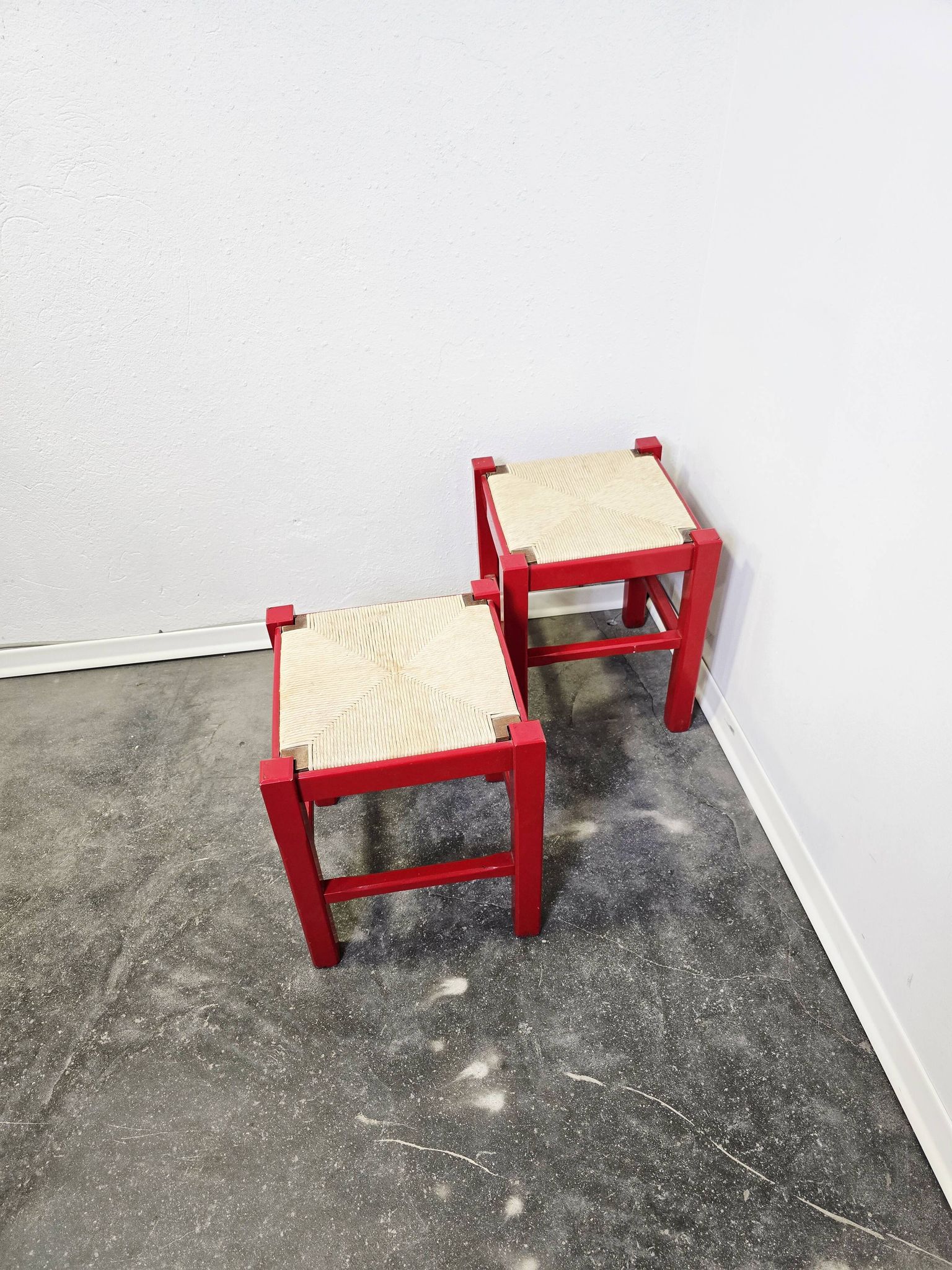 Red wooden stool with a woven straw seat.