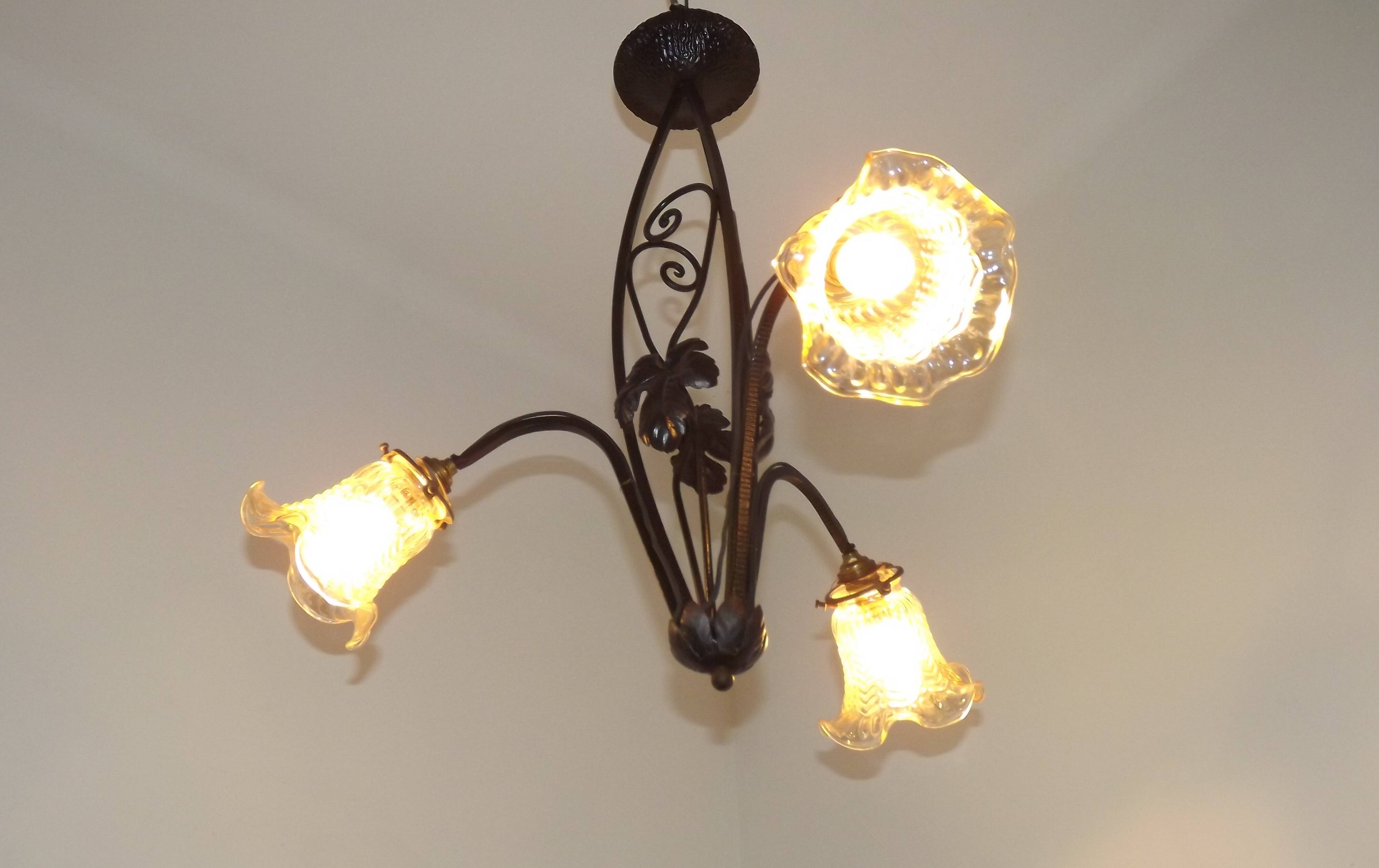 French Art Nouveau leaf detail iron three-light chandelier with amber glass shades.