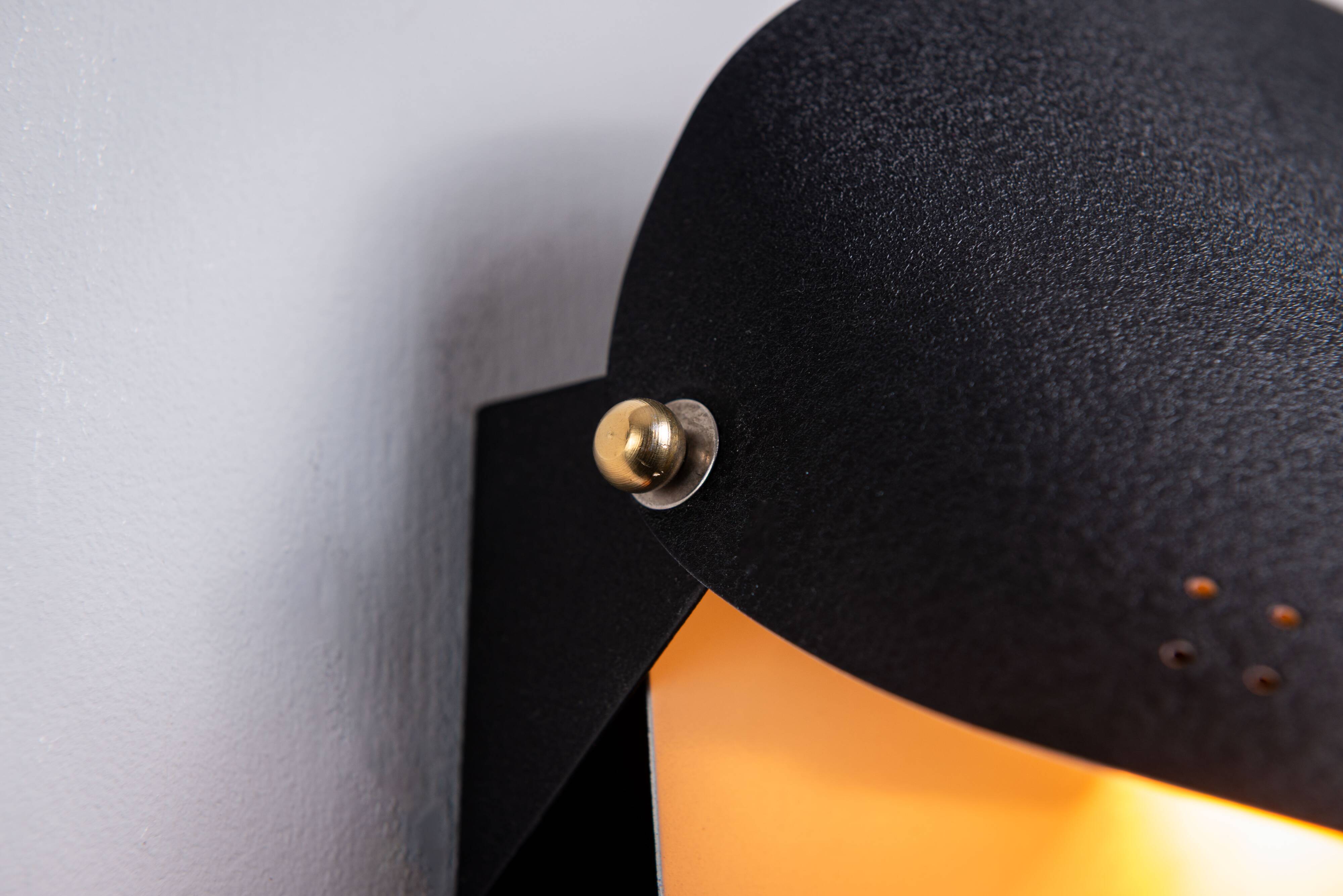 Matte black wall lamps with perforated shades and brass details