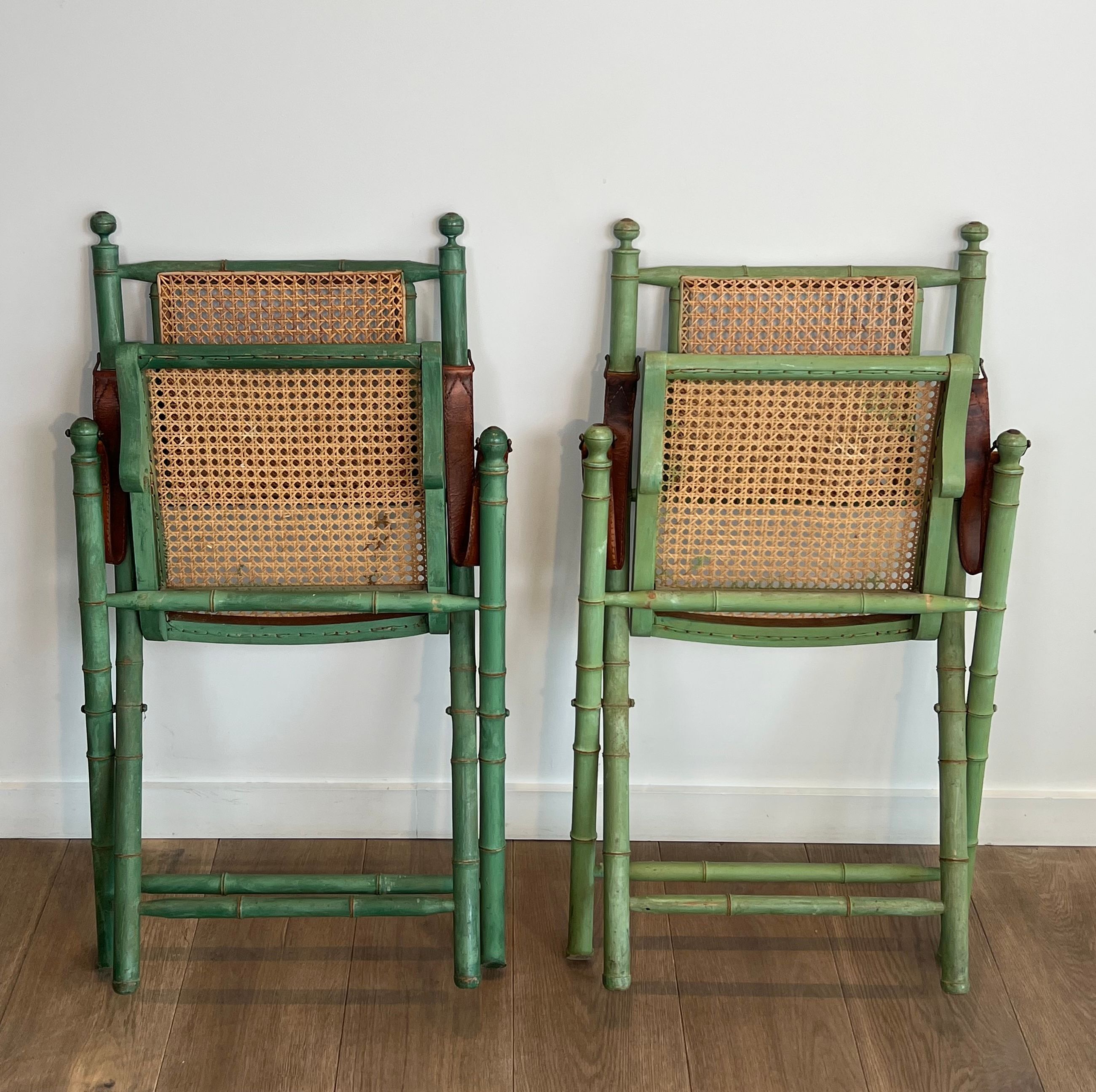 Paire de chaises safari pliantes façon faux-bambou patiné, dossiers et assises cannées et repose-bras en cuir