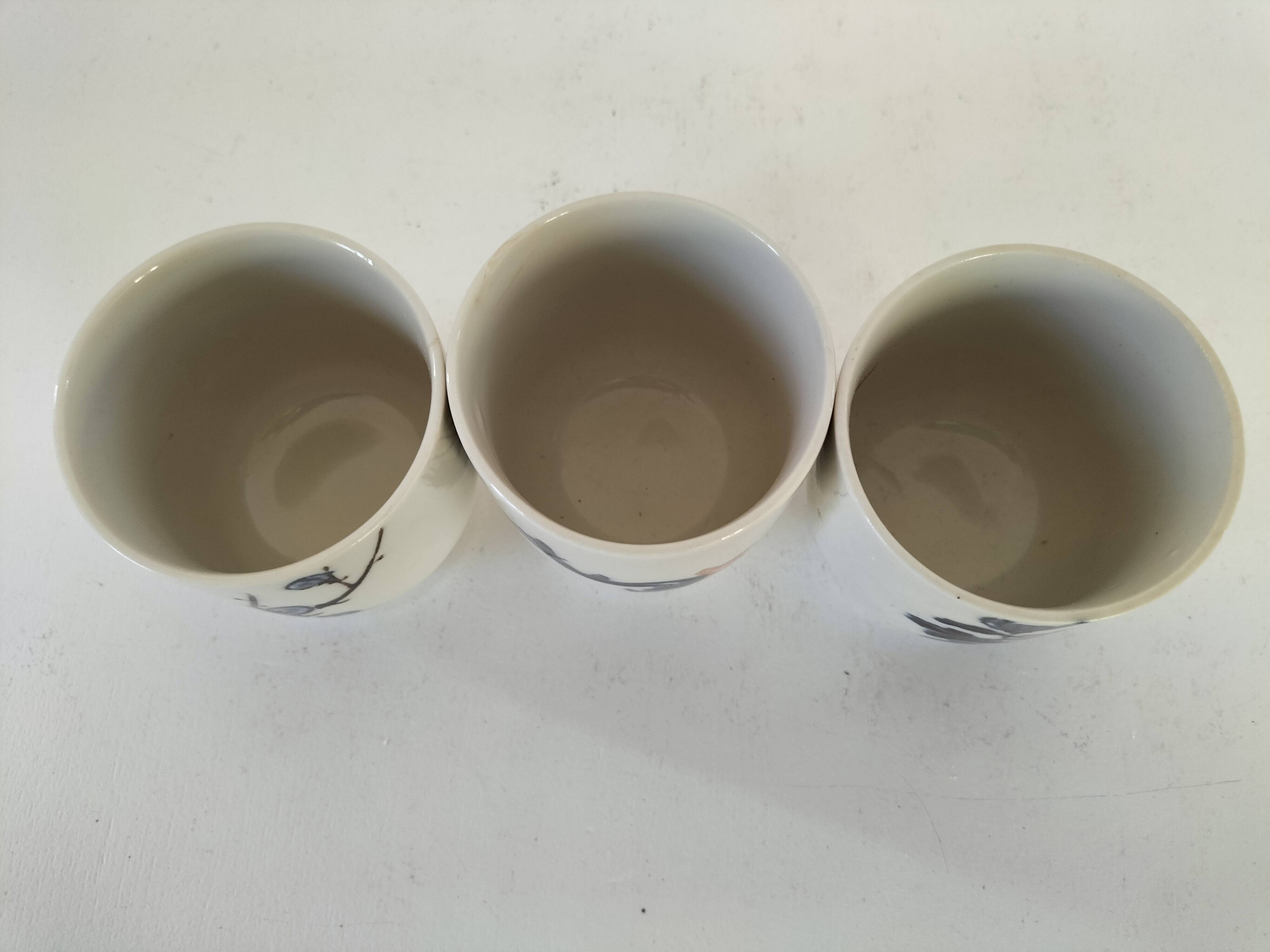Set of three hand-painted porcelain cups with floral patterns.