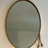 Oval brass mirror surrounded by a cord and adorned