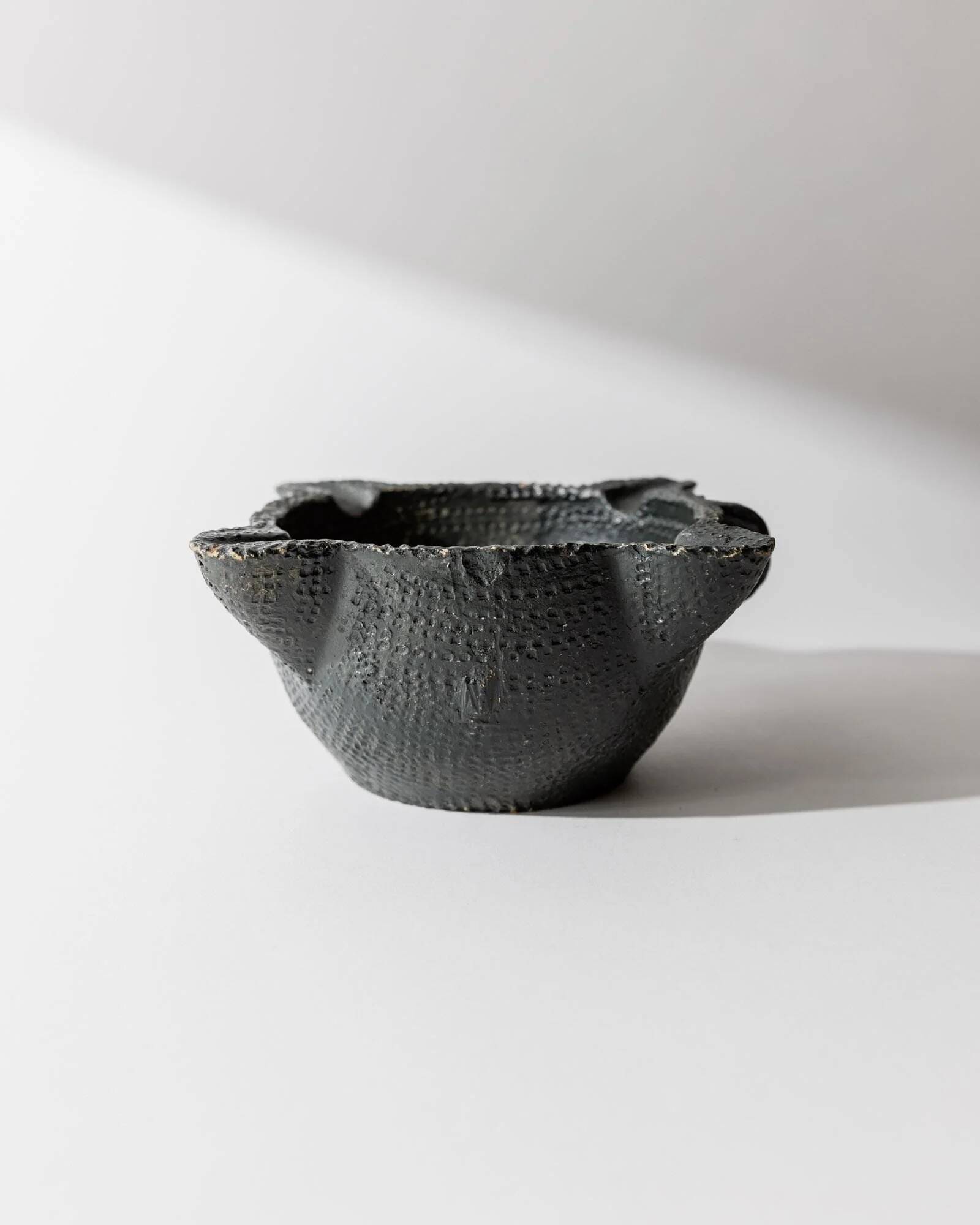 Vintage ceramic ashtray from the 1960s, black, hand-sculpted texture, organic shape.