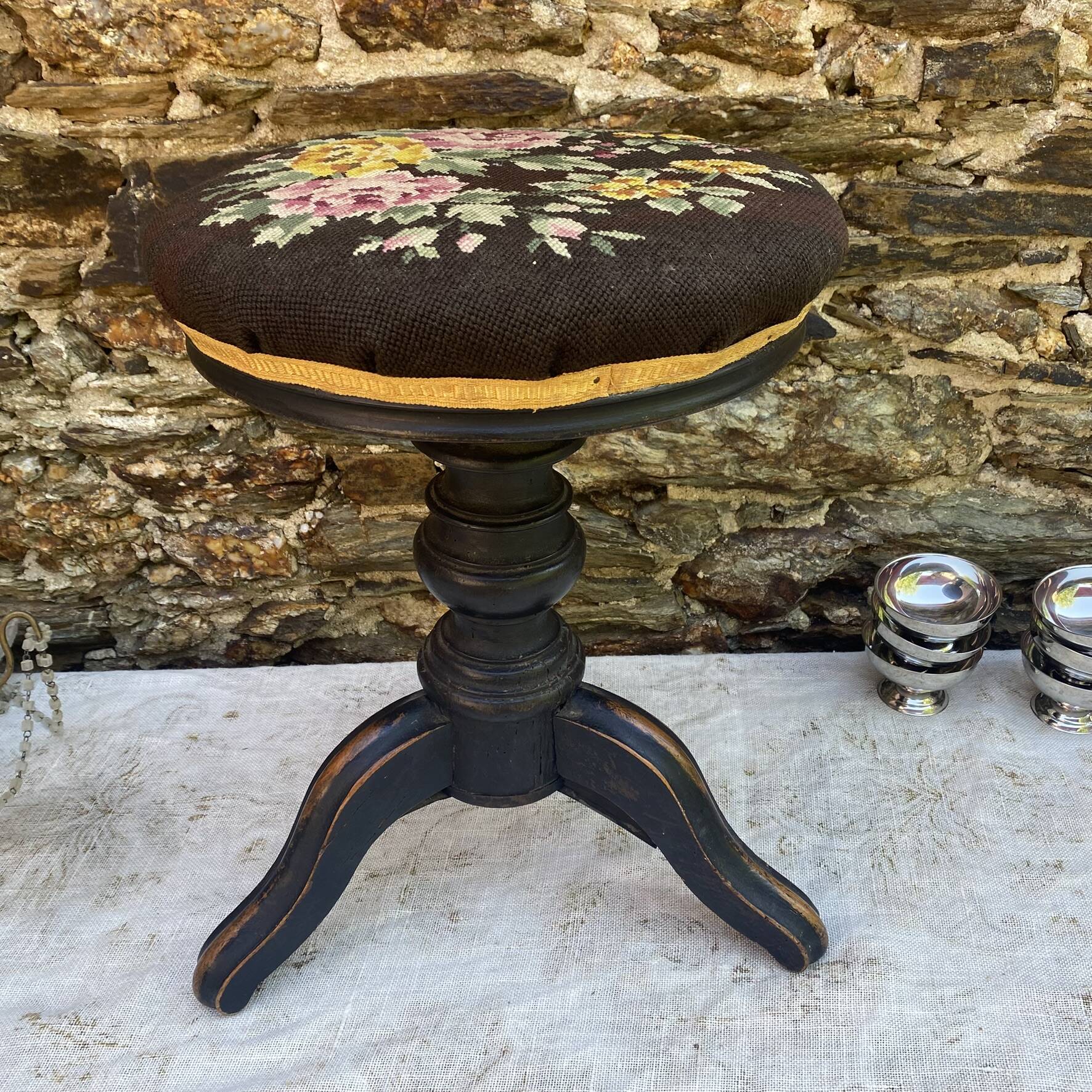 Old adjustable piano stool, blackened wood, metal screws, embroidered seat.