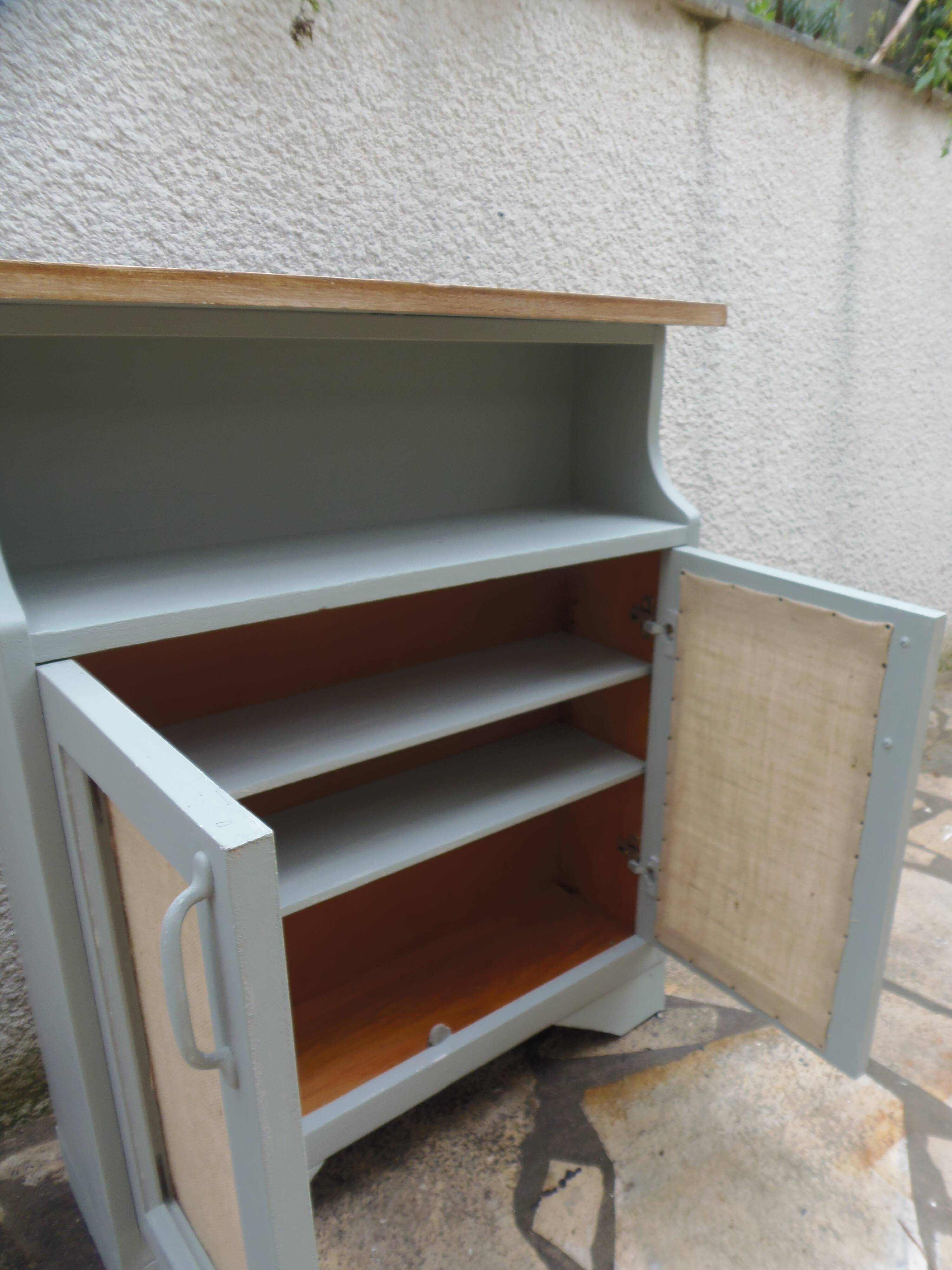 Small vintage green-grey piece of furniture, with 2 doors covered in burlap.