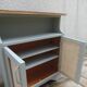 Small vintage green-grey piece of furniture, with 2 doors covered in burlap.