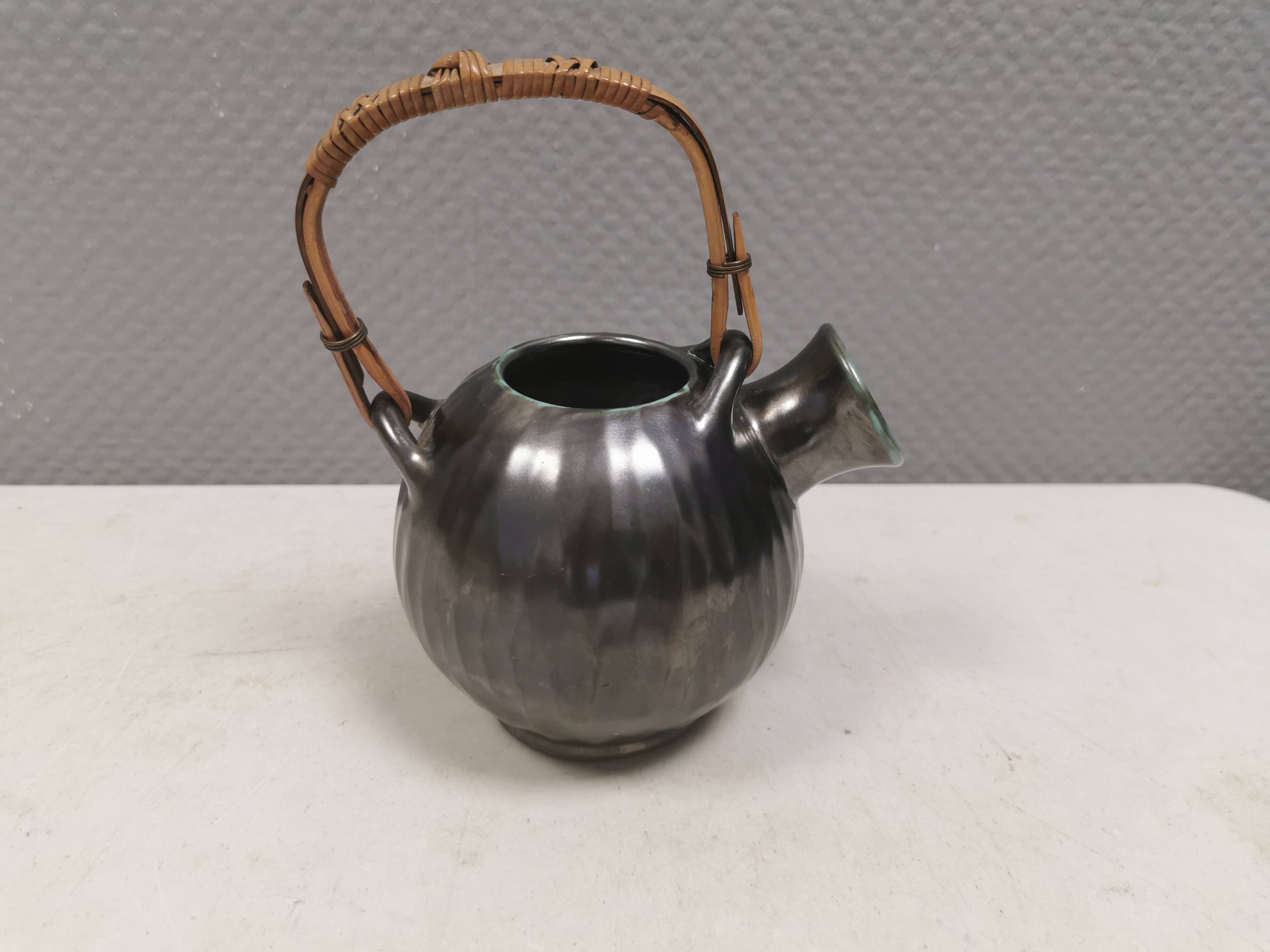 A ceramic jug with a metallic glaze and a handle made of woven raffia.