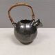A ceramic jug with a metallic glaze and a handle made of woven raffia.