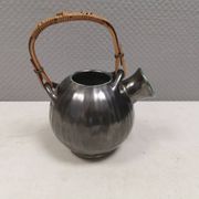 A ceramic jug with a metallic glaze and a handle made of woven raffia.