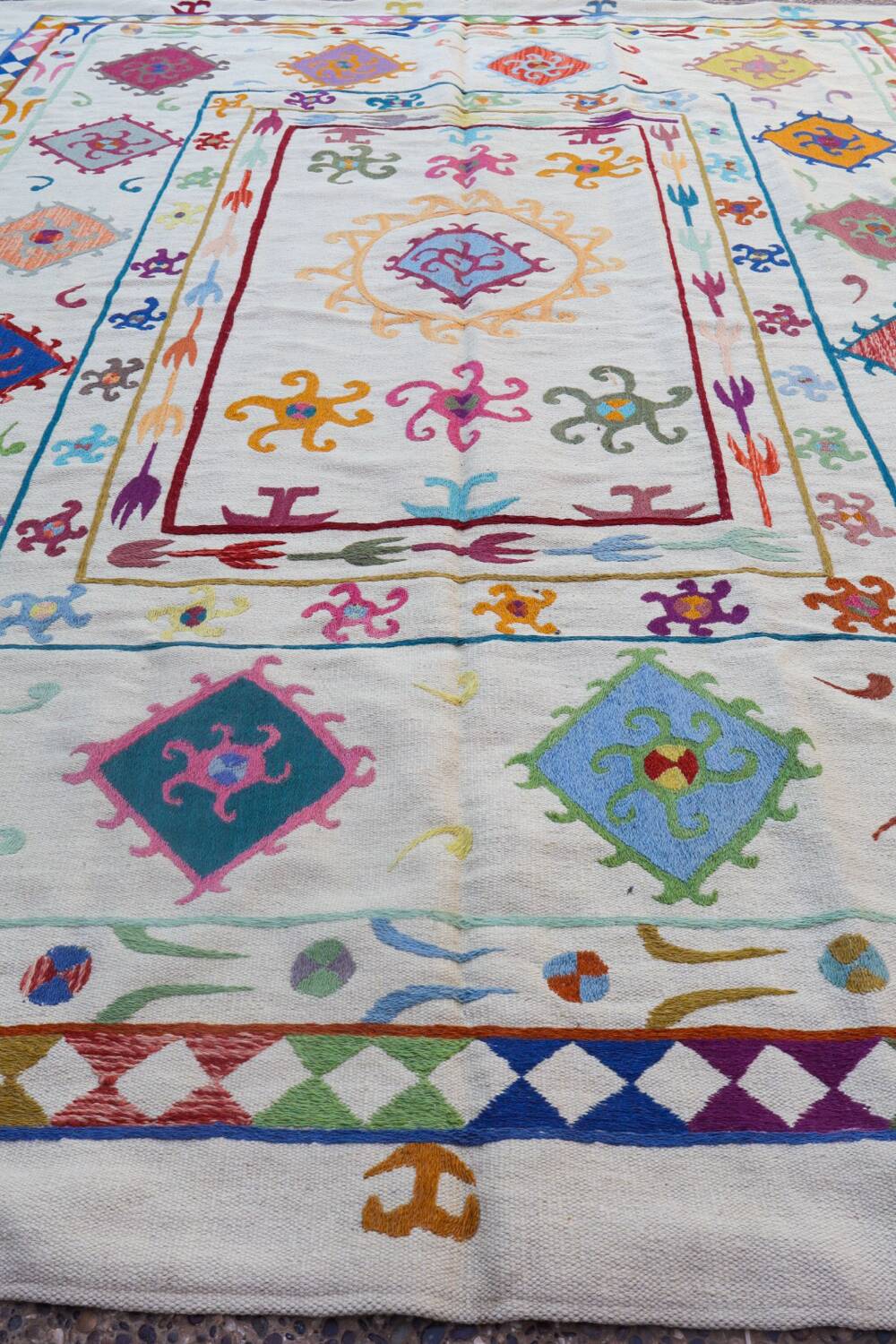 White suzani kilim rug with multi-colored embroidered patterns