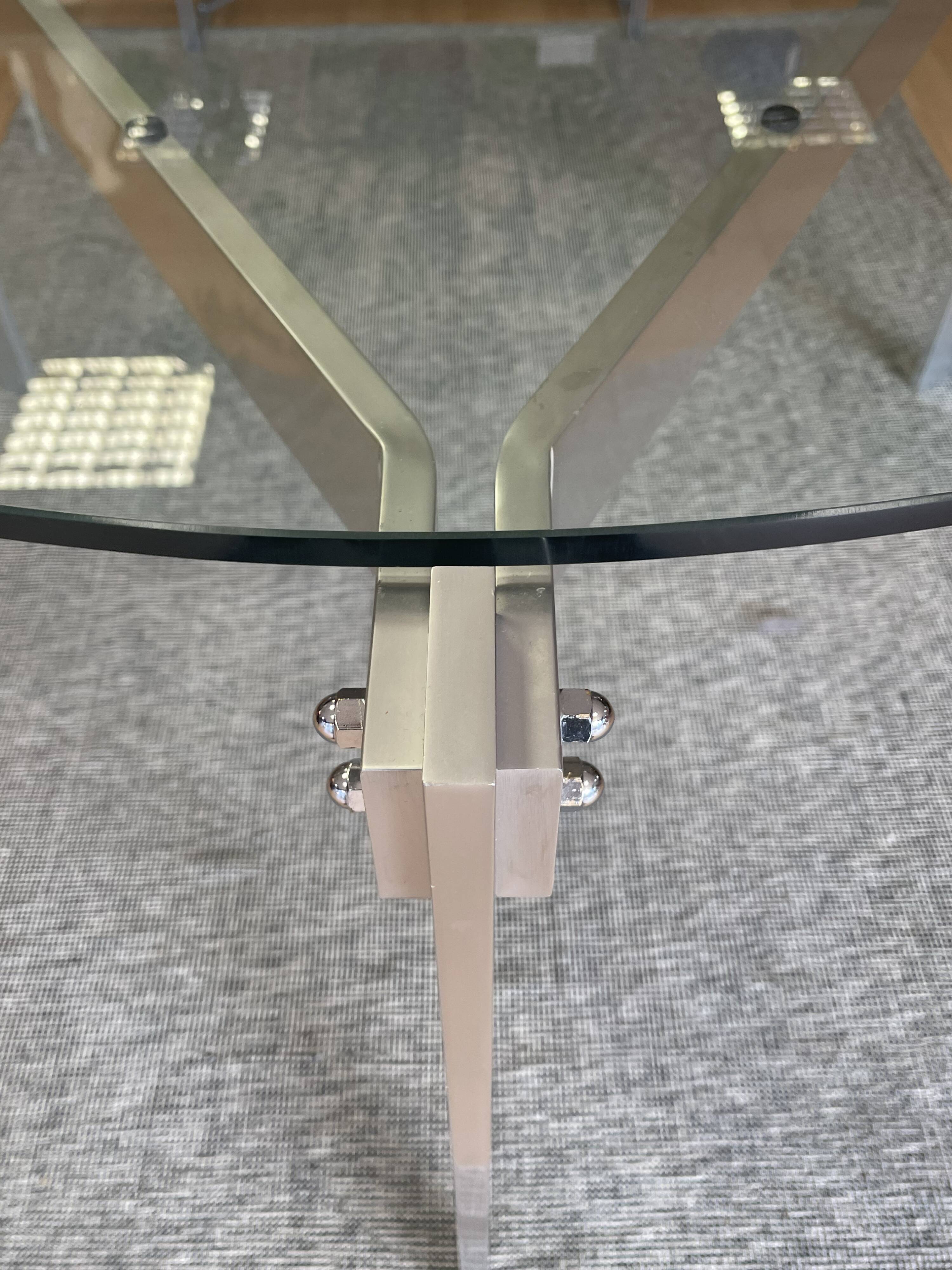 Round dining table with a glass top and brushed metal triangular frame.