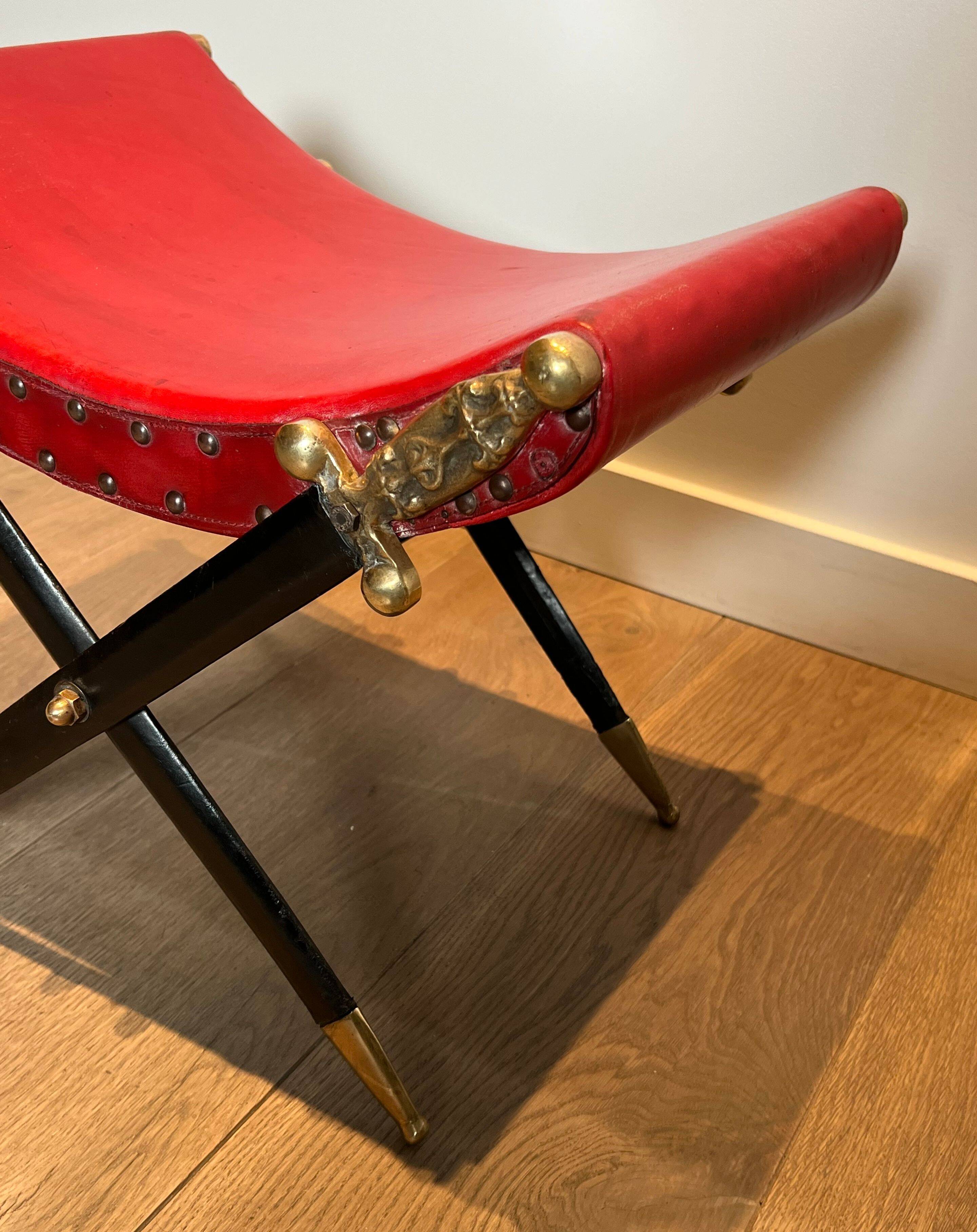 Neoclassical curule stool in red leather, decorated with crossed swords in bronze and metal covered in black leather.