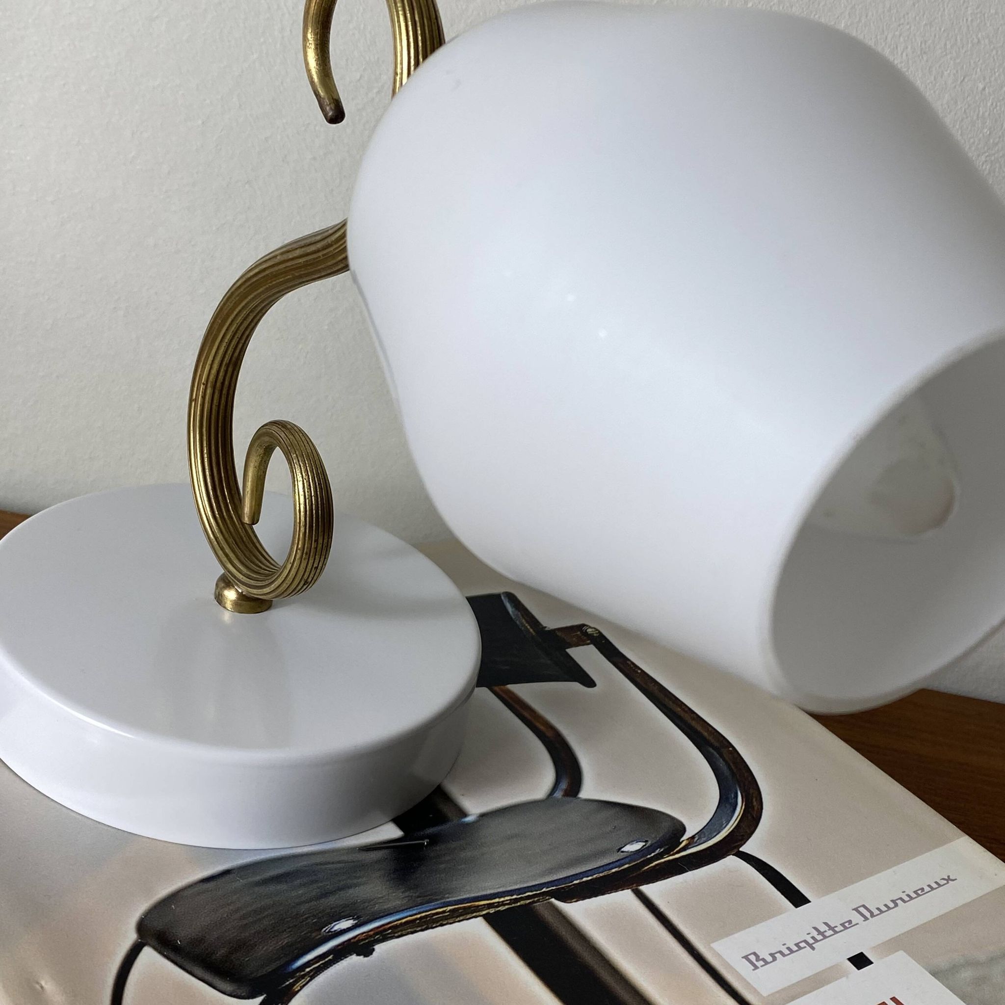 Swan neck wall light in brass with a white glass shade.