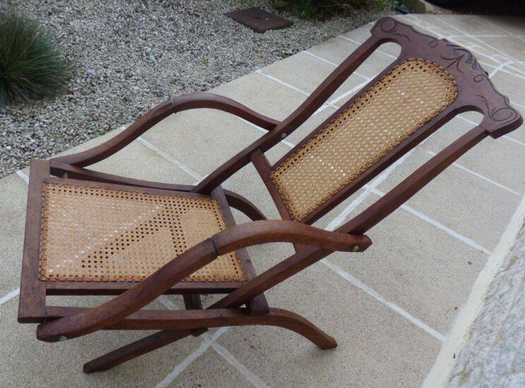 Antique folding chair with caned seat and backrest made of wood.