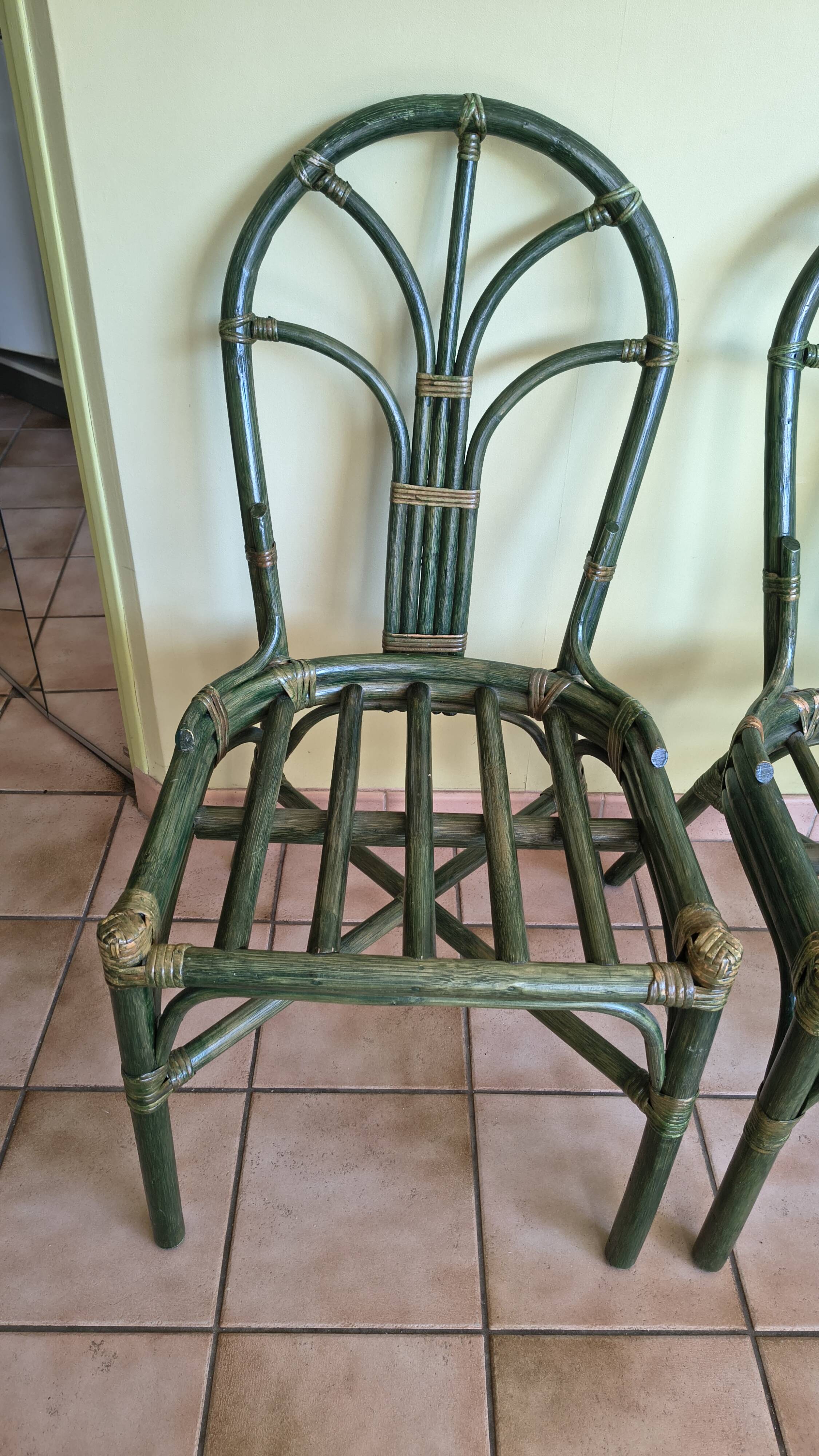 Round rattan table with glass top and 4 green rattan chairs.