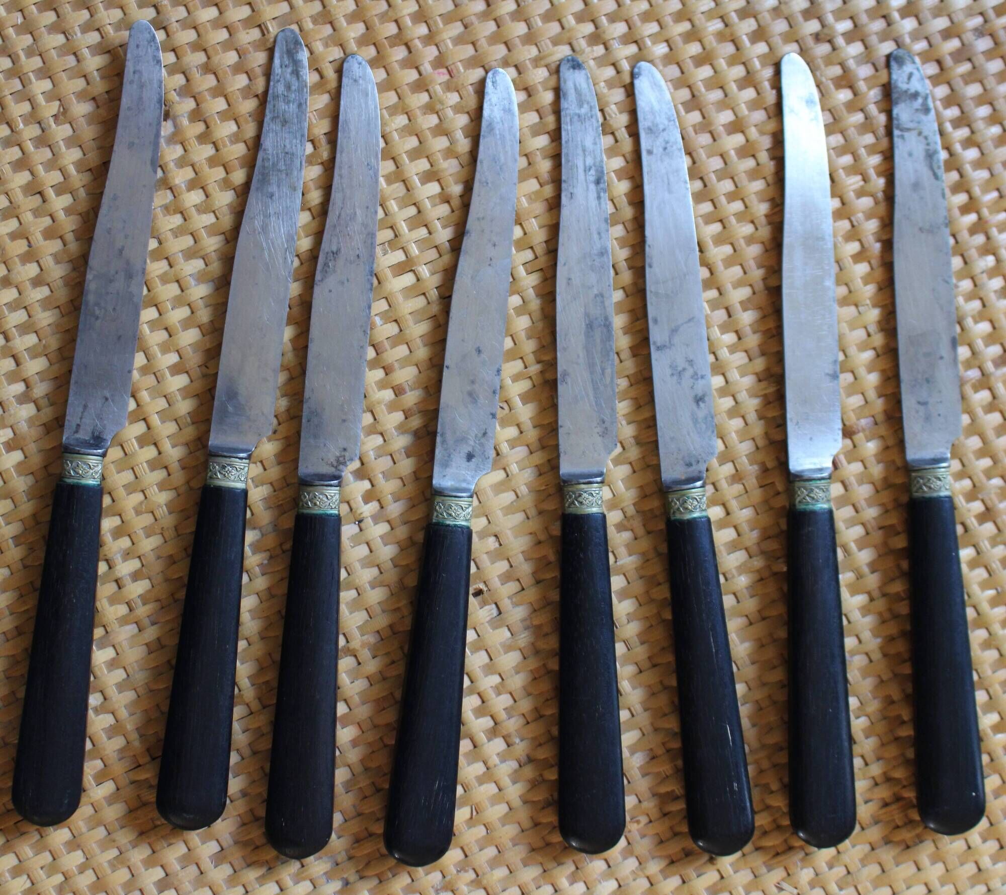 A set of 8 knives with black wooden handles and bolsters.