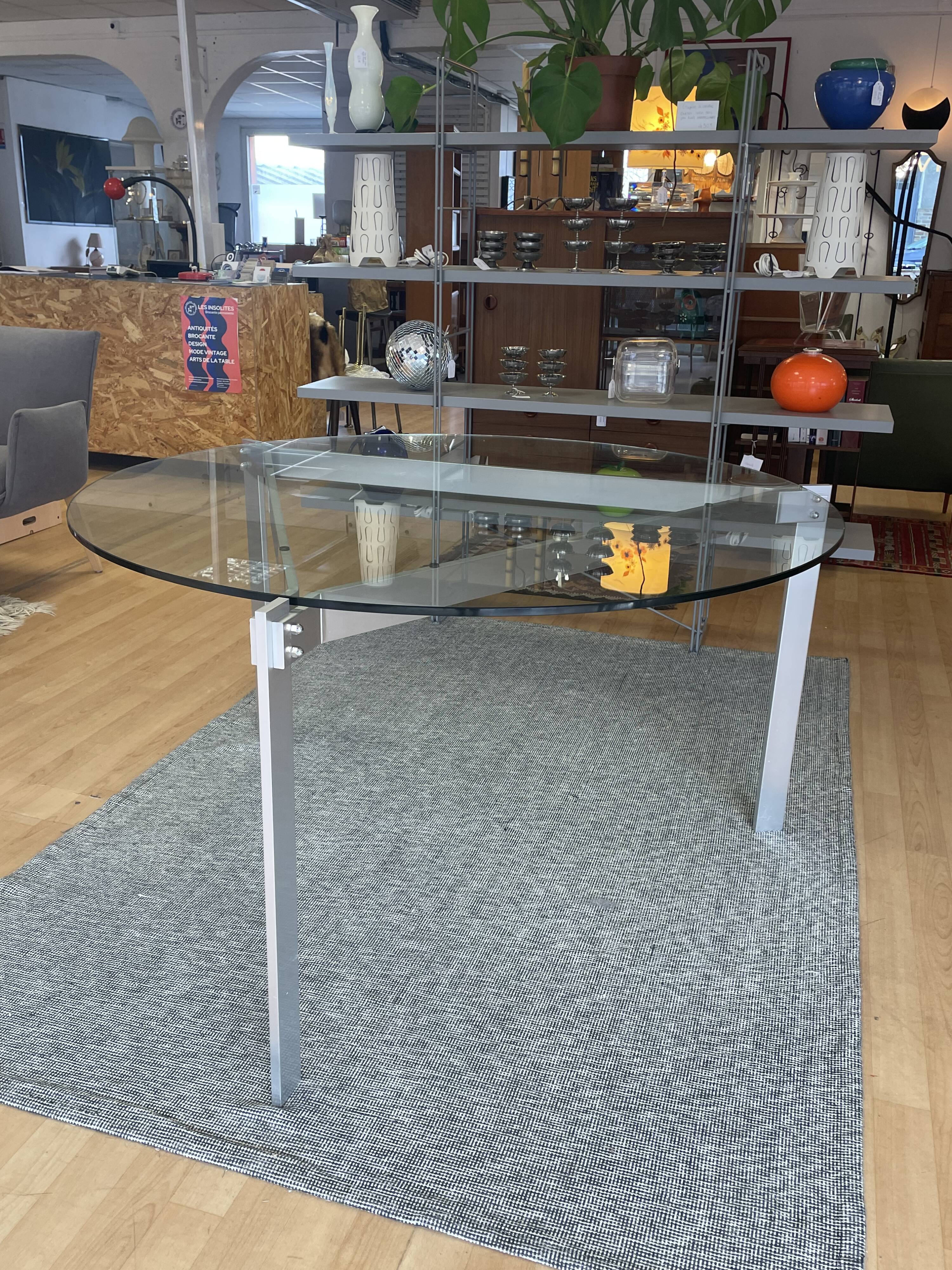 Round dining table with a glass top and brushed metal triangular frame.