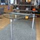 Round dining table with a glass top and brushed metal triangular frame.