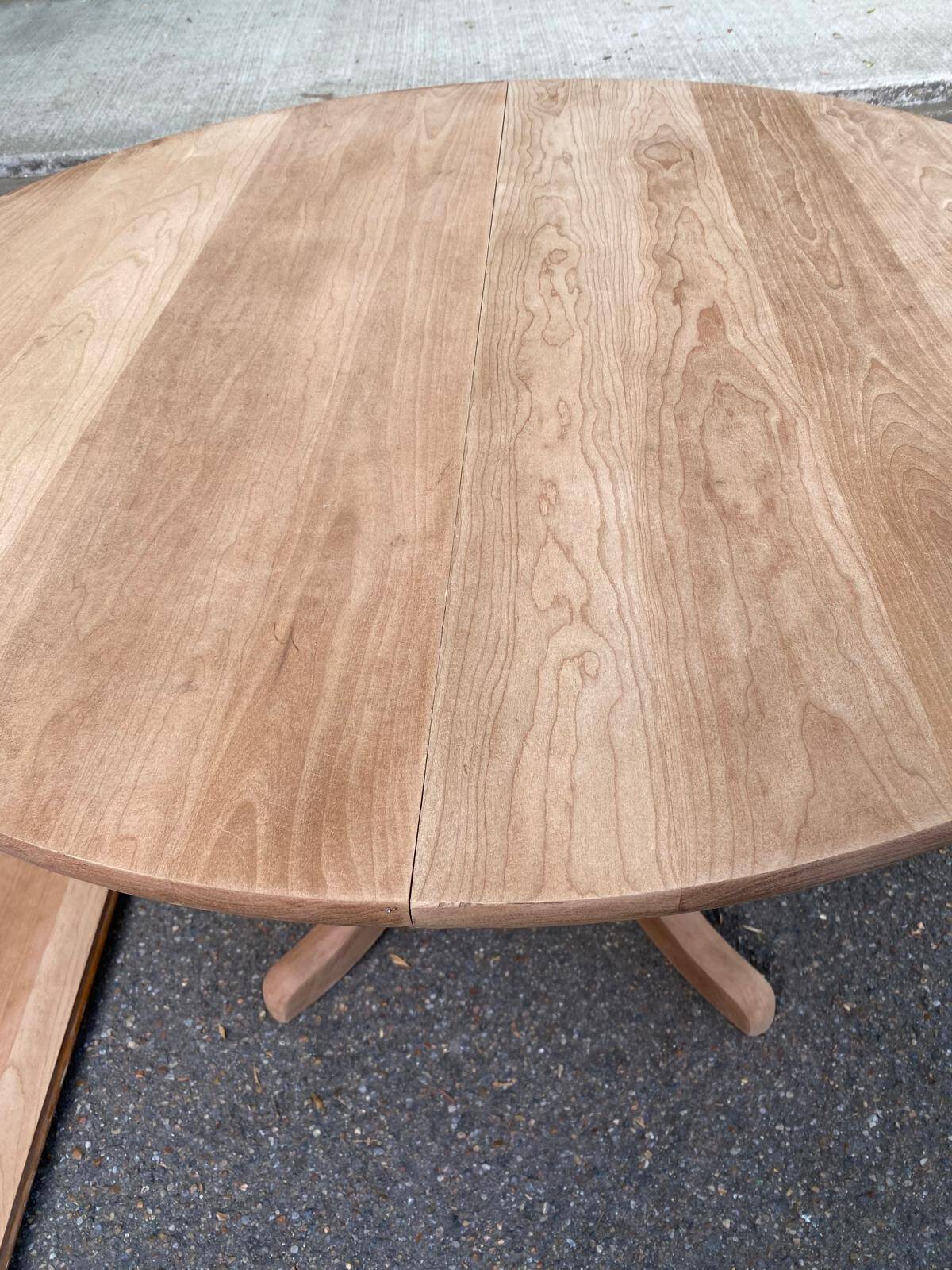 Large extendable round dining table stripped in solid cherry wood with a central leg.