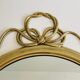 Decorative oval mirror in brass adorned with a large twisted bow.