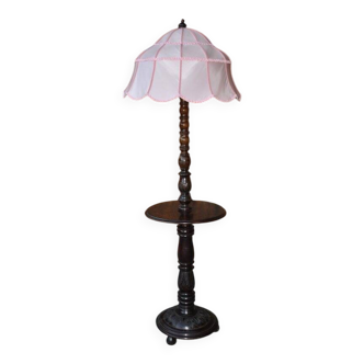 Brown carved wooden floor lamp with a pale pink shade and integrated shelf.
