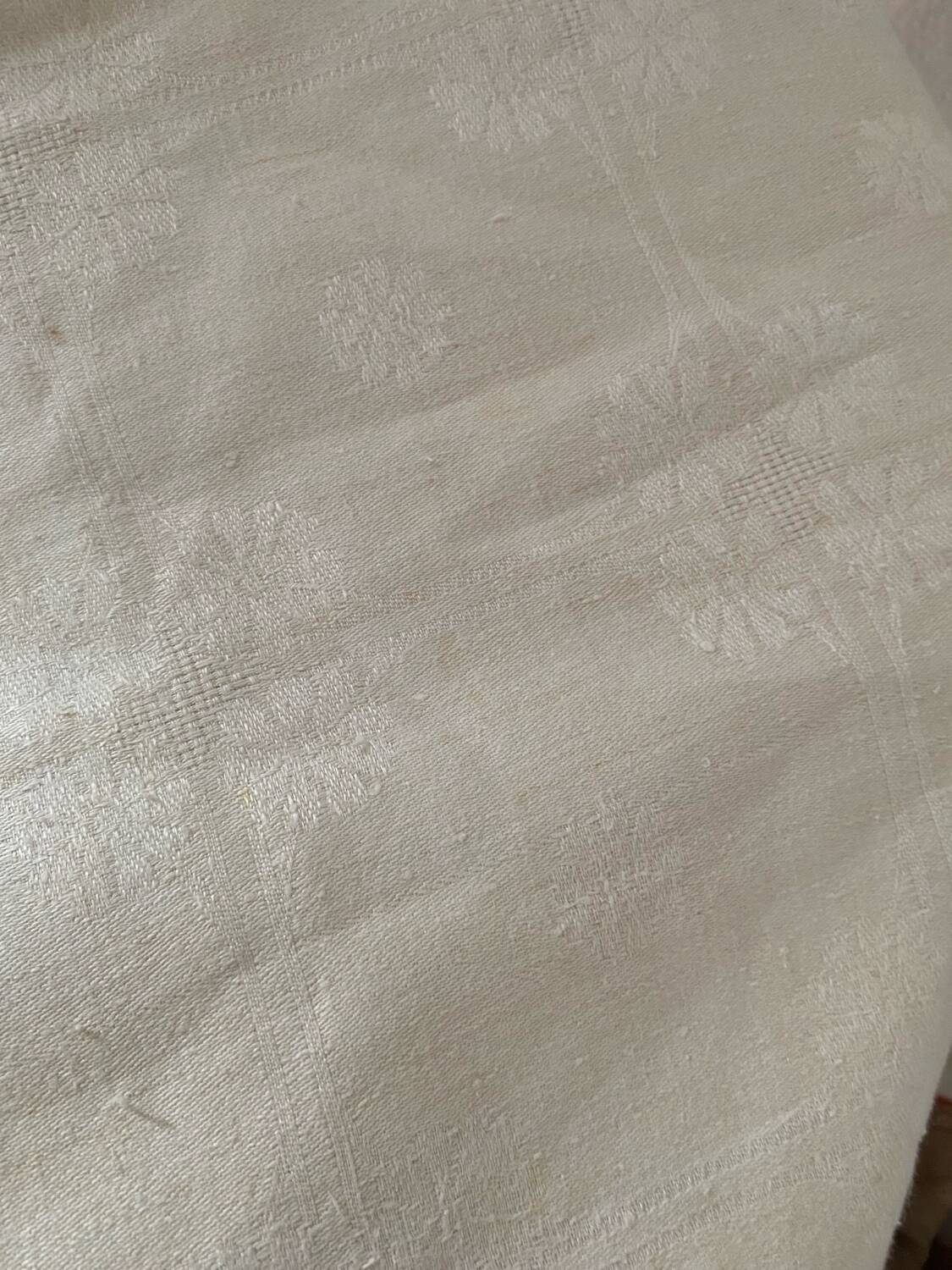 Damask tablecloth with a floral pattern and a central embroidered monogram.