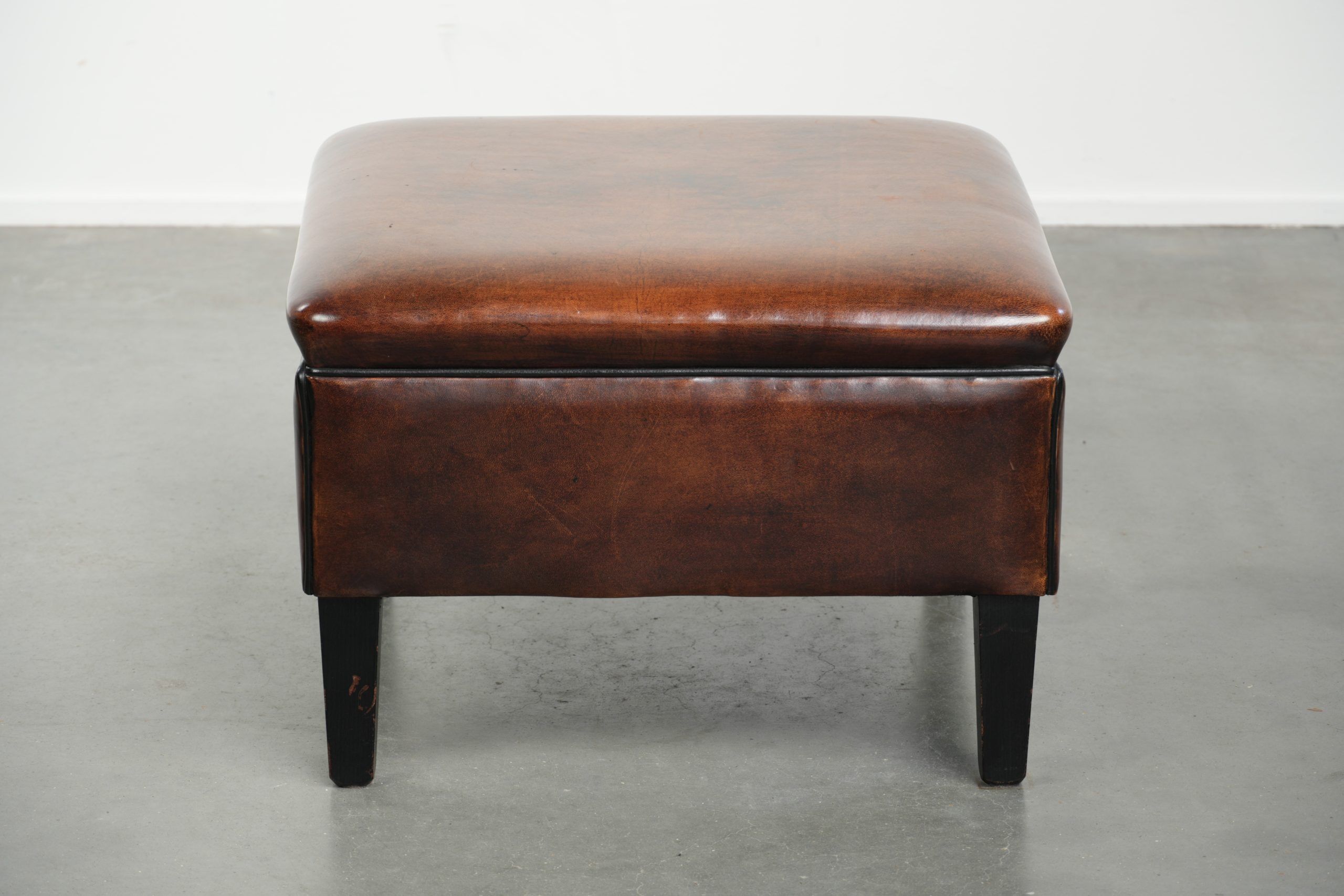 Large dark brown square ottoman made of sheepskin with black piping