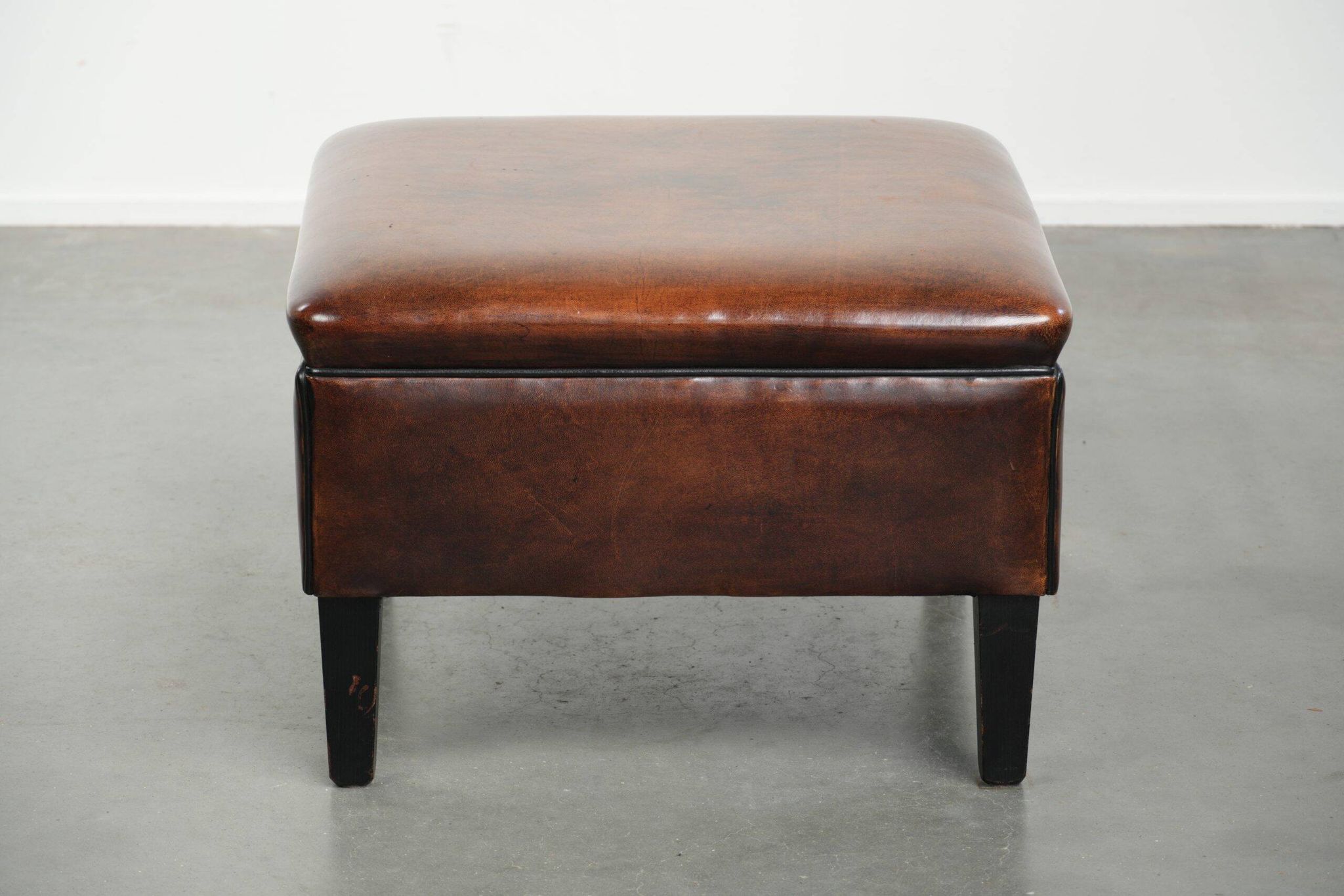 Pouf carré marron foncé en peau de mouton avec un passepoil noir.