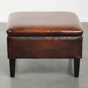 Pouf carré marron foncé en peau de mouton avec un passepoil noir.