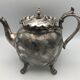 Old teapot pourer in silver metal decorated with foliage and butterflies