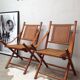 Pair of folding chairs in bamboo and caning, leather and brass