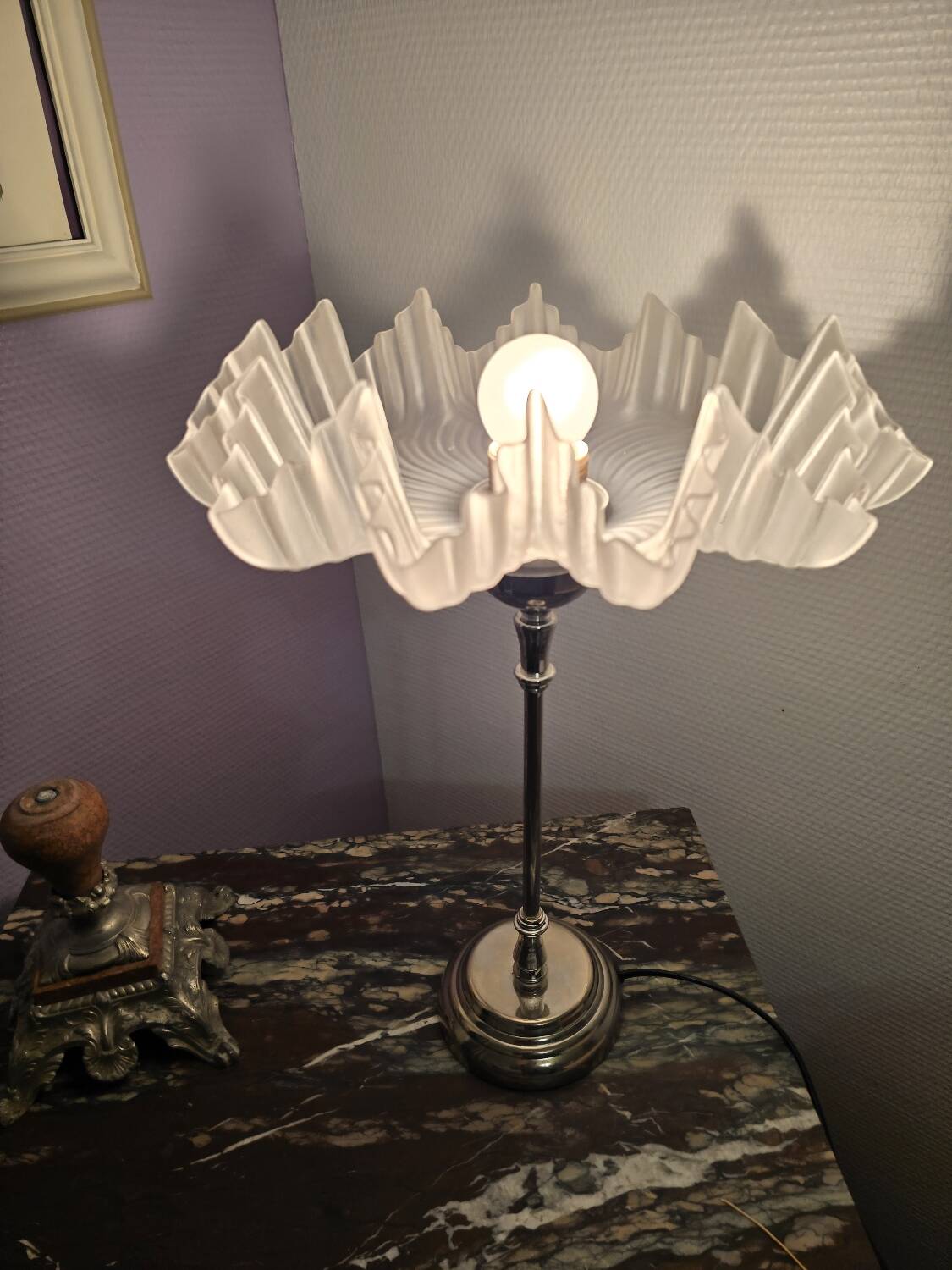 Table lamp with a silver base and a scalloped shade.