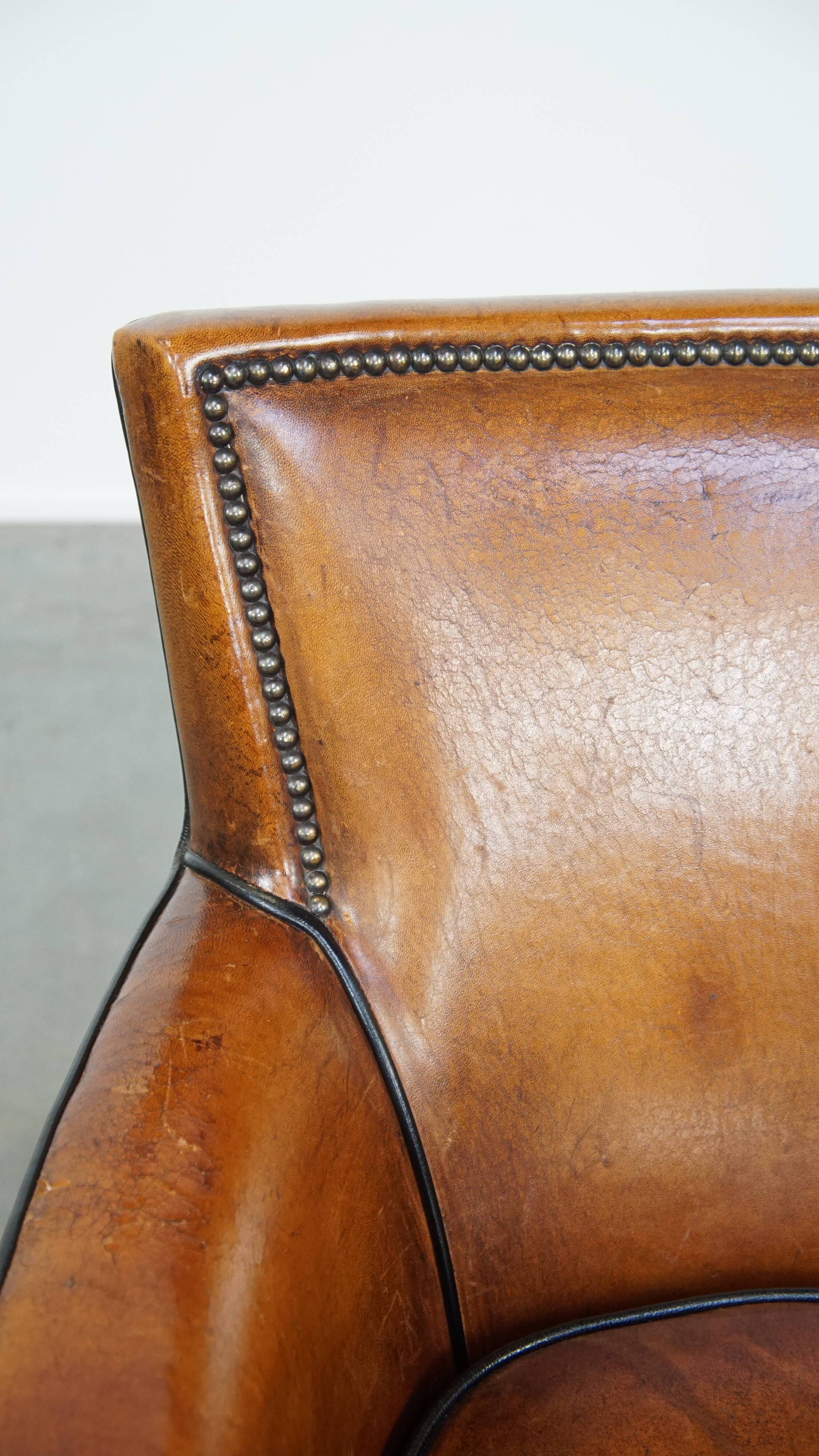 Cognac-colored sheepskin armchair with black piping and decorative nails