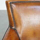 Cognac-colored sheepskin armchair with black piping and decorative nails