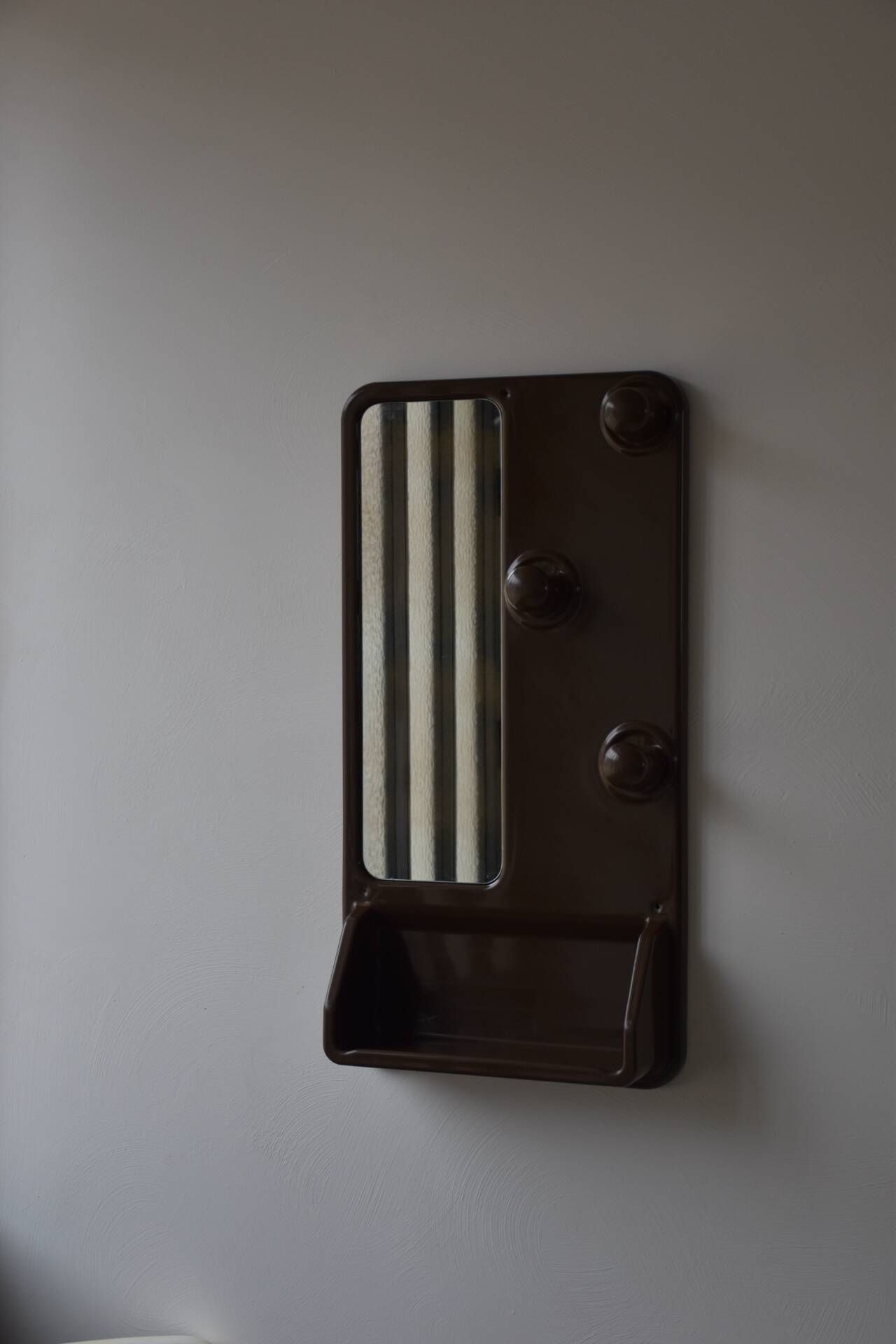 Wall mirror in moulded plastic with hooks and shelf.