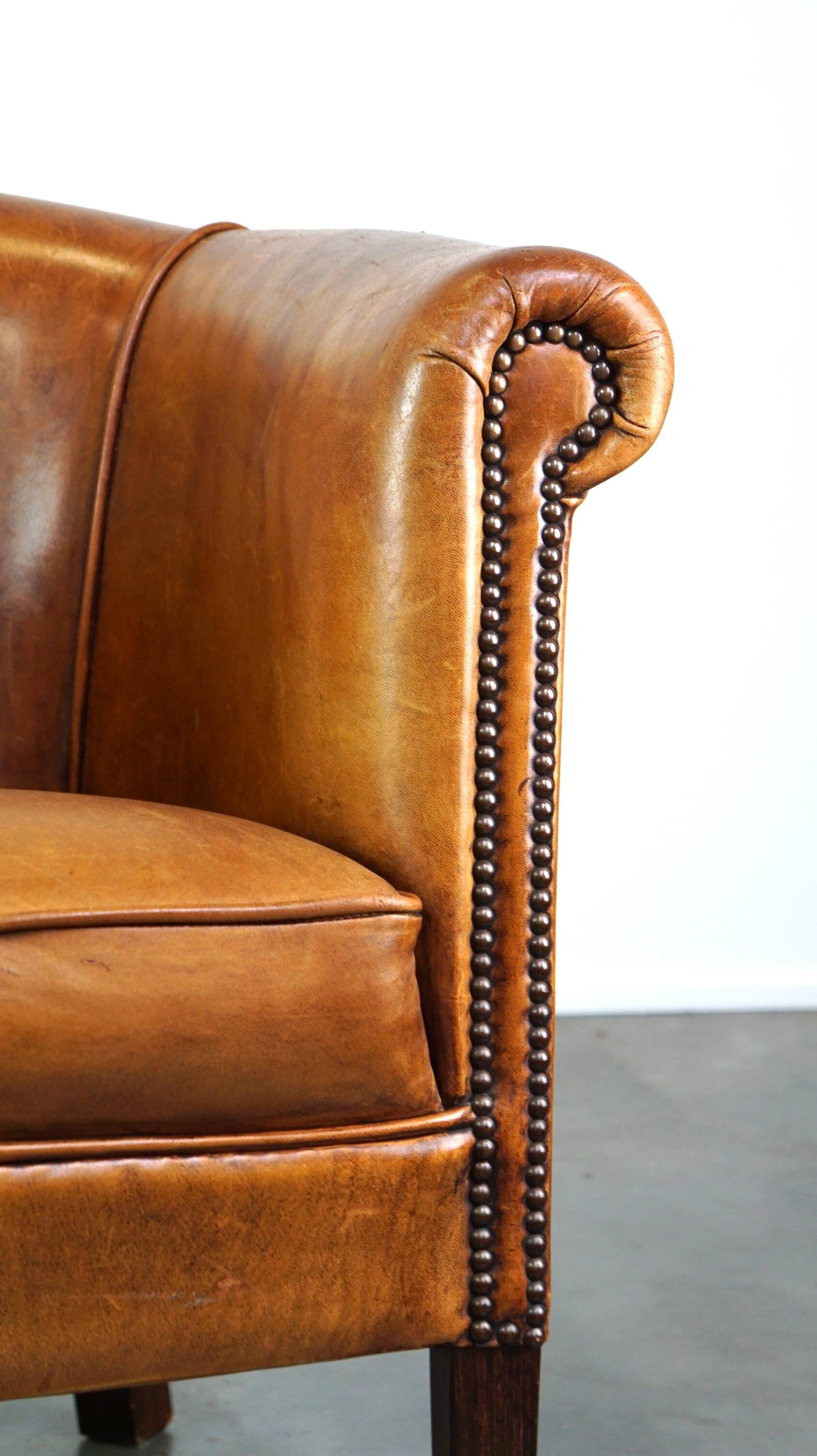 Neat and subtle sheepskin club chair, finished with decorative studs and a fixed seat cushion