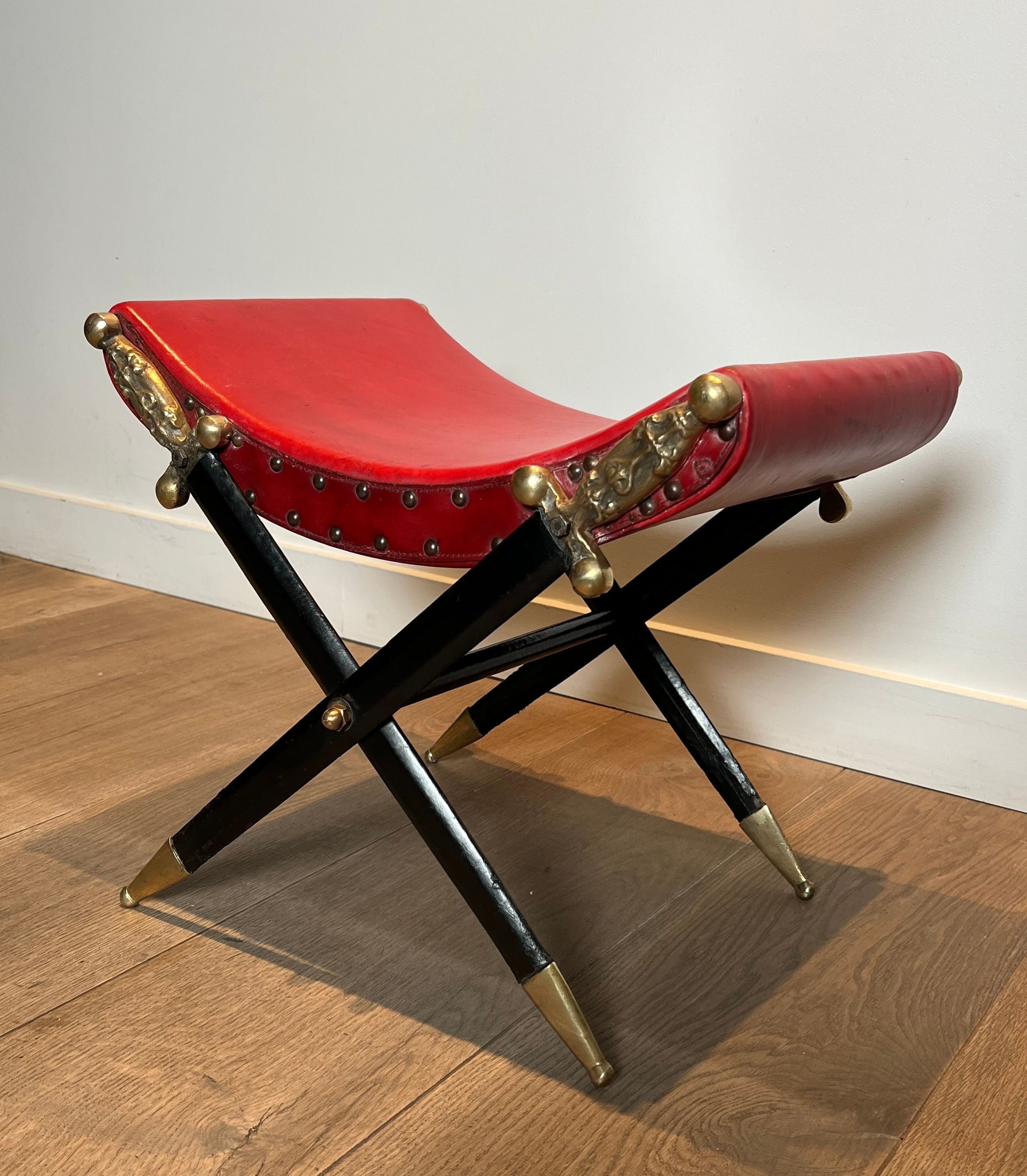 Neoclassical curule stool in red leather, decorated with crossed swords in bronze and metal covered in black leather.